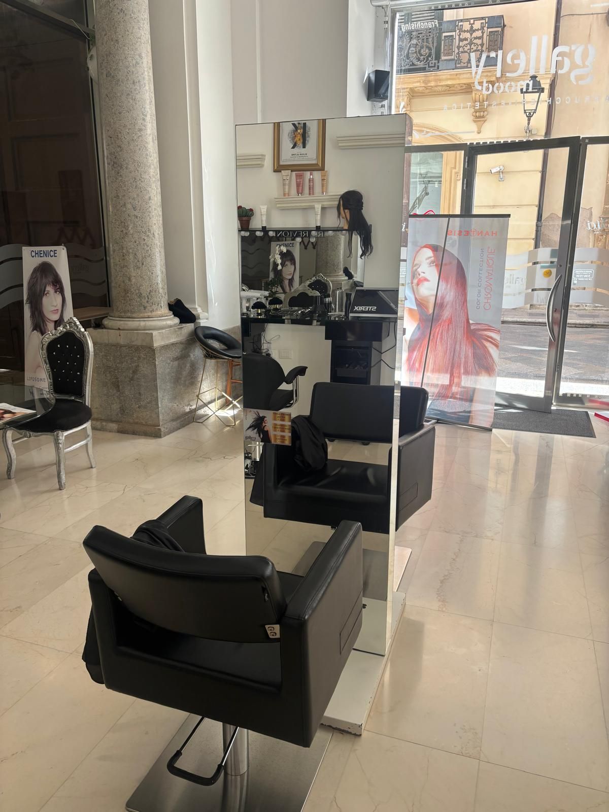 Interni moderni di un salone con poltrone da parrucchiere, specchi e ingresso in vetro.