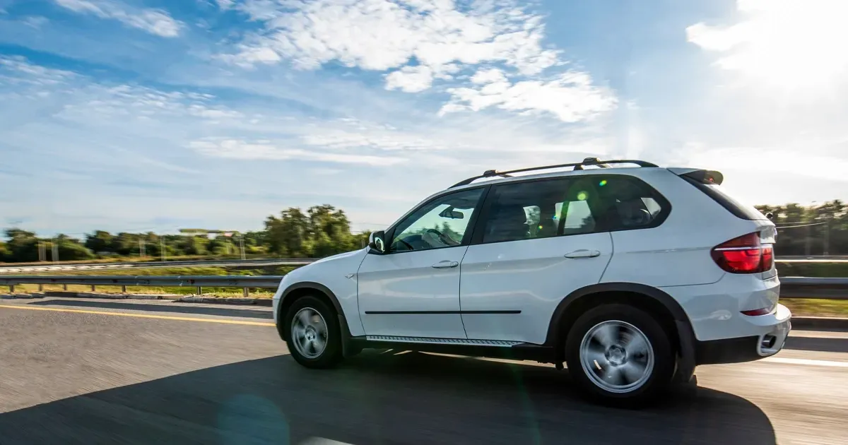 White SUV driving on a sunny road beside a field and blue sky | Burke View Garage