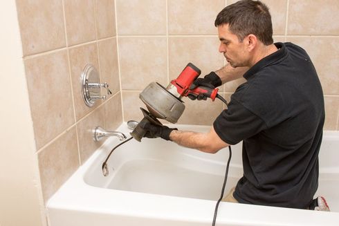 Plumber cleaning a drain in a bathtub.