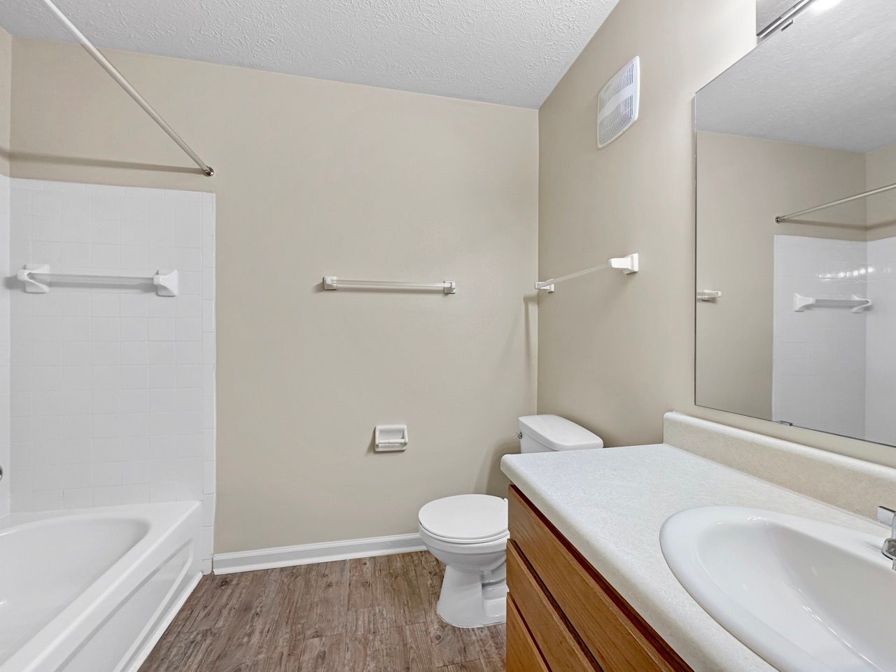 Bathroom with a white tub and toilet, neutral walls, and a wooden vanity.