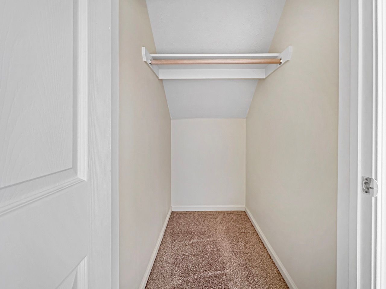 Small empty closet with a shelf, rod, and carpet. Beige walls and white trim.