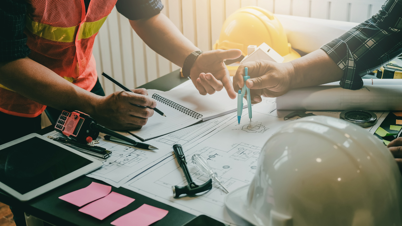 two construction workers are looking at a blueprint with a compass