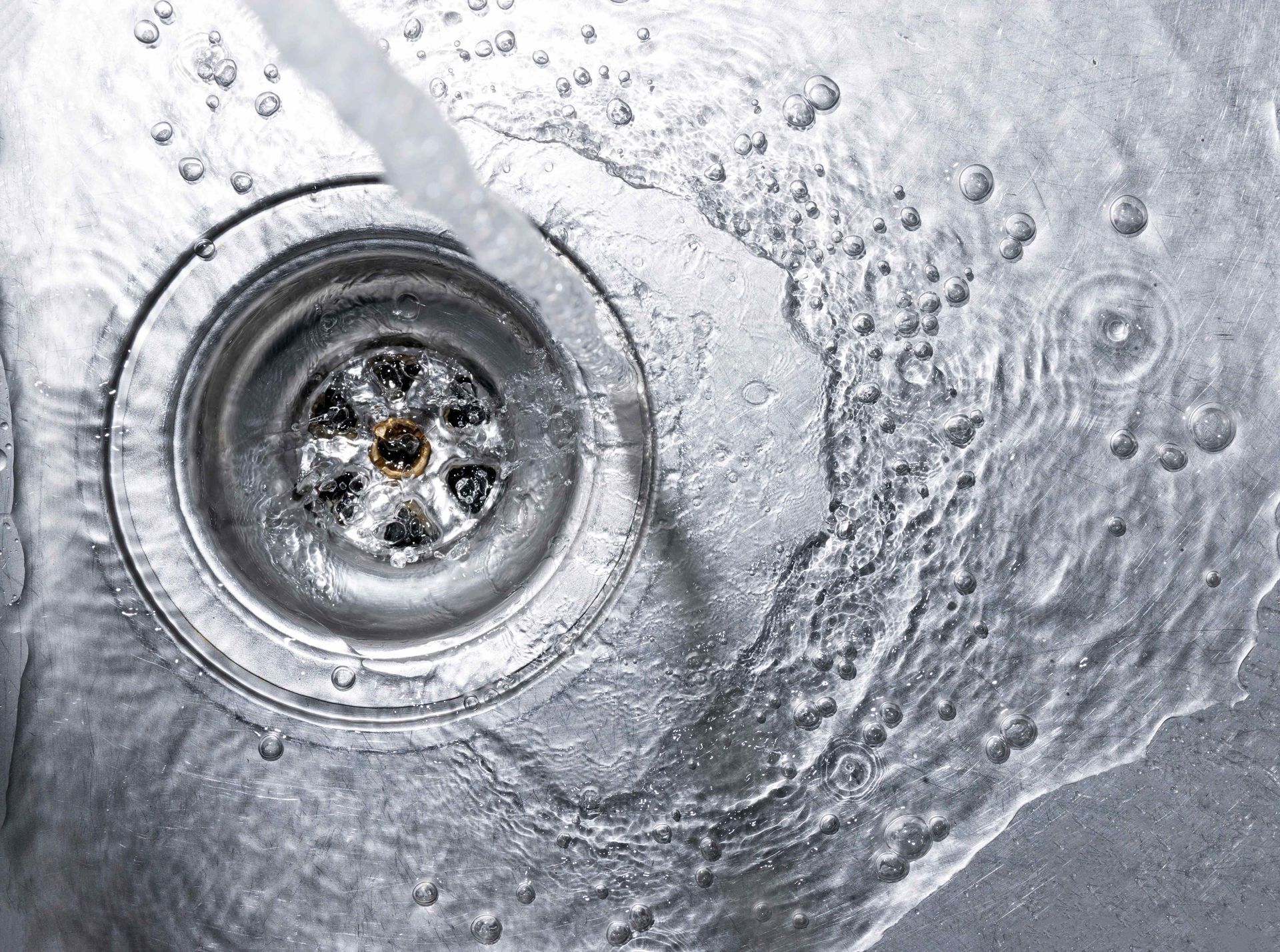 Chrome sink drain with water swirling around the circular basin