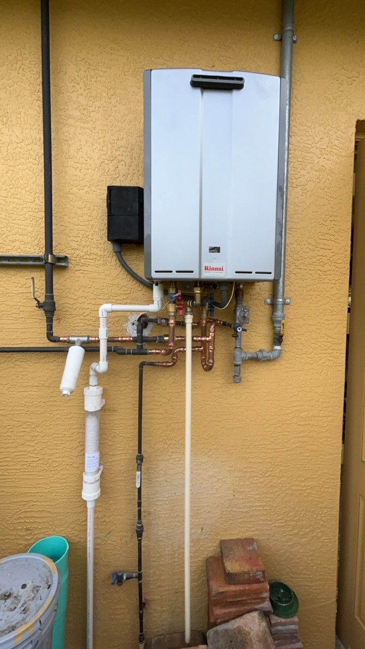 White water heater mounted on blue tiled bathroom wall, with pipes and valves underneath