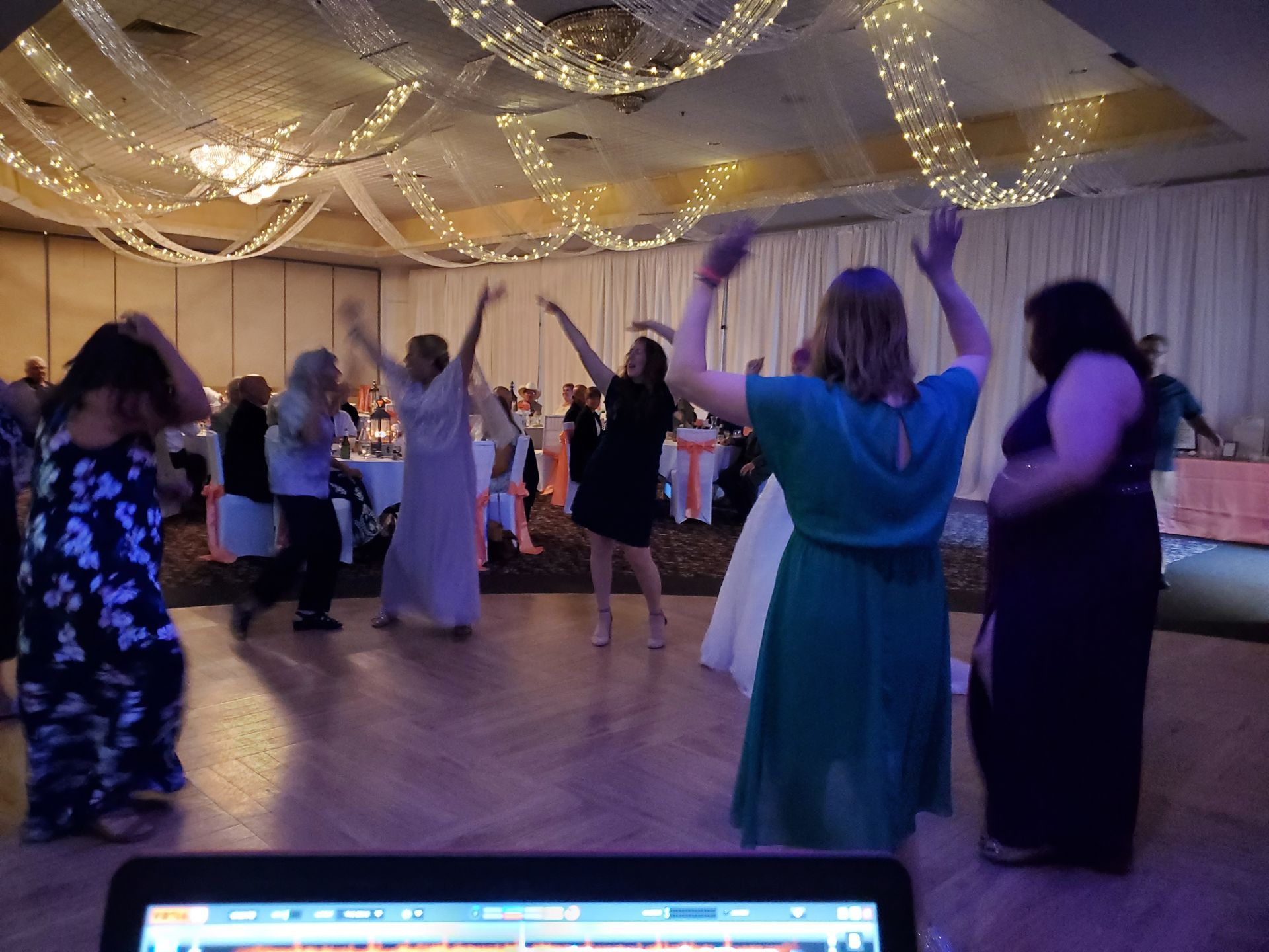 A group of people are dancing in a large room at a wedding reception.