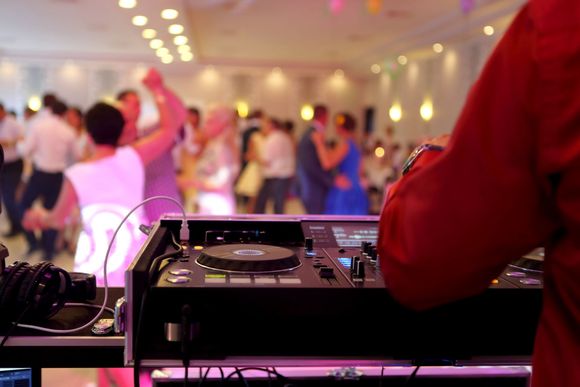 A dj is playing music at a party with a crowd of people dancing in the background.