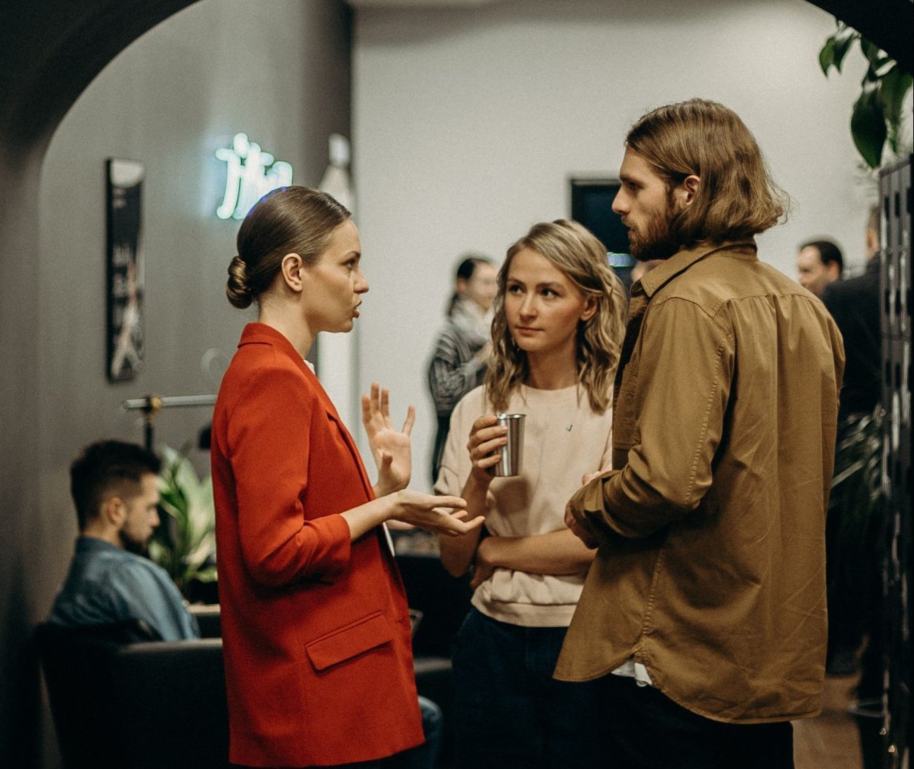 A woman in a red jacket is talking to two other people