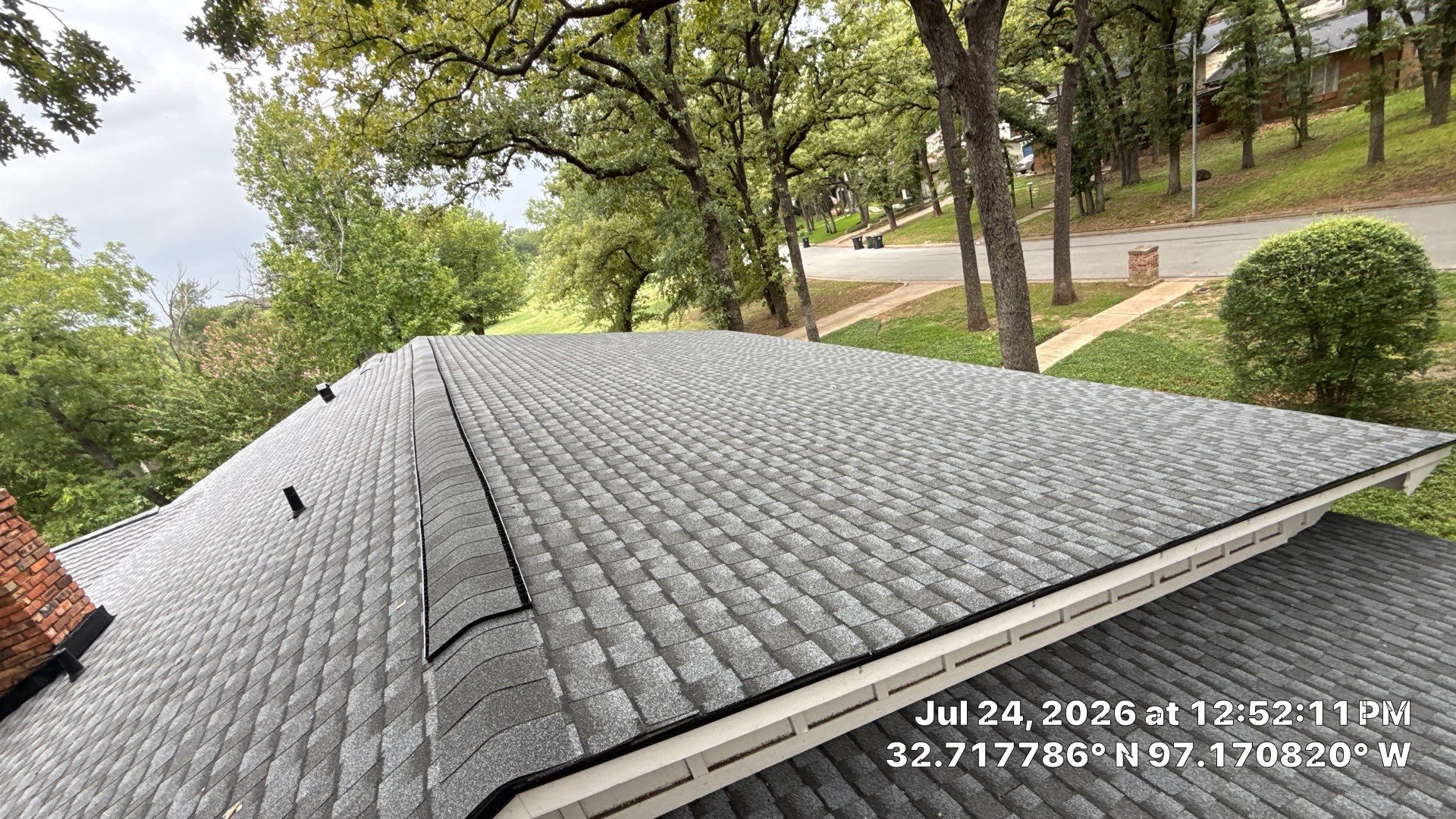 Gray shingled roof with trees and a road beyond, seen from above