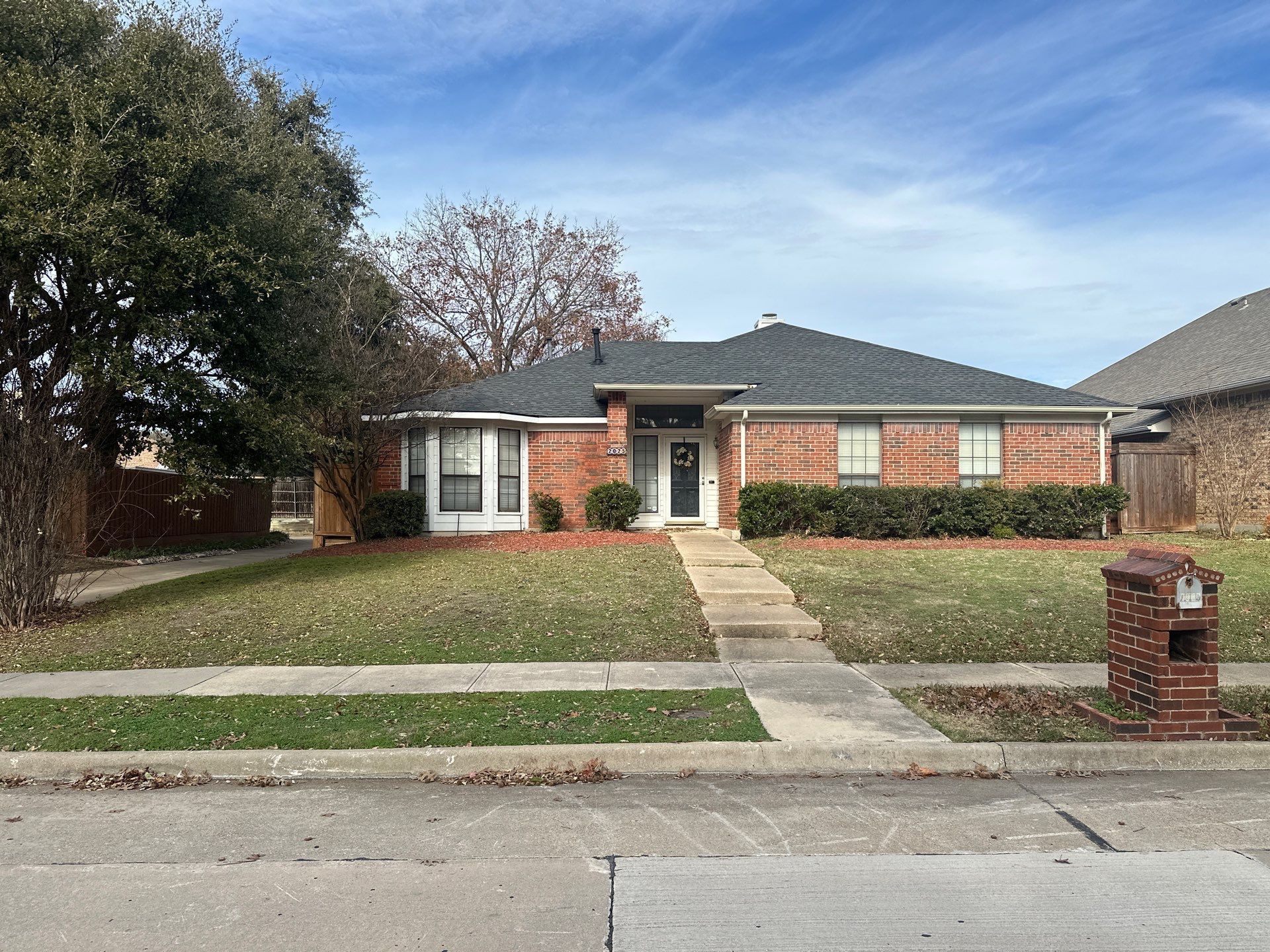 Single-story brick house with a front lawn, walkway, and mailbox on a quiet suburban street