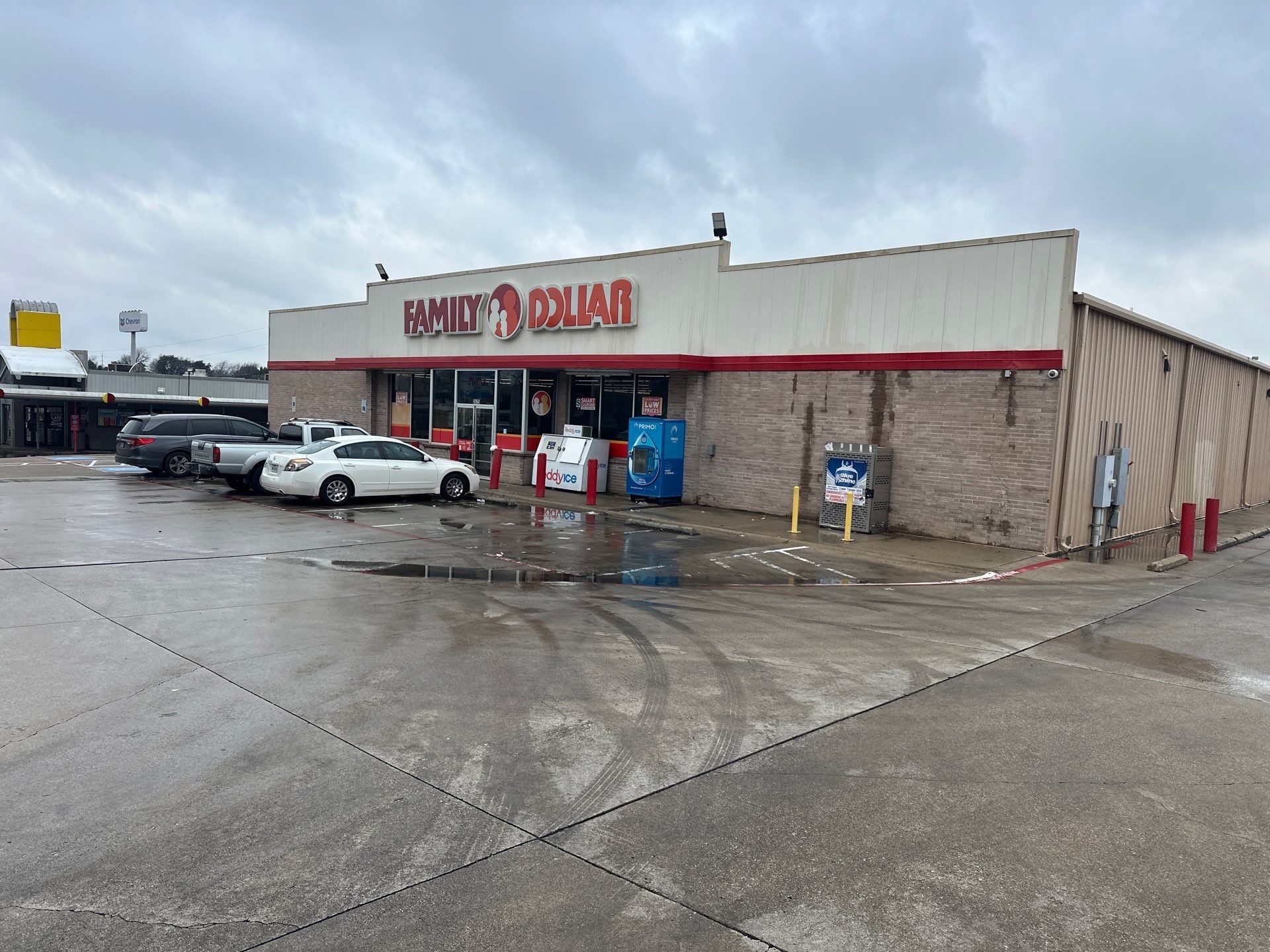 Convenience store exterior on a rainy day with parked cars and wet pavement