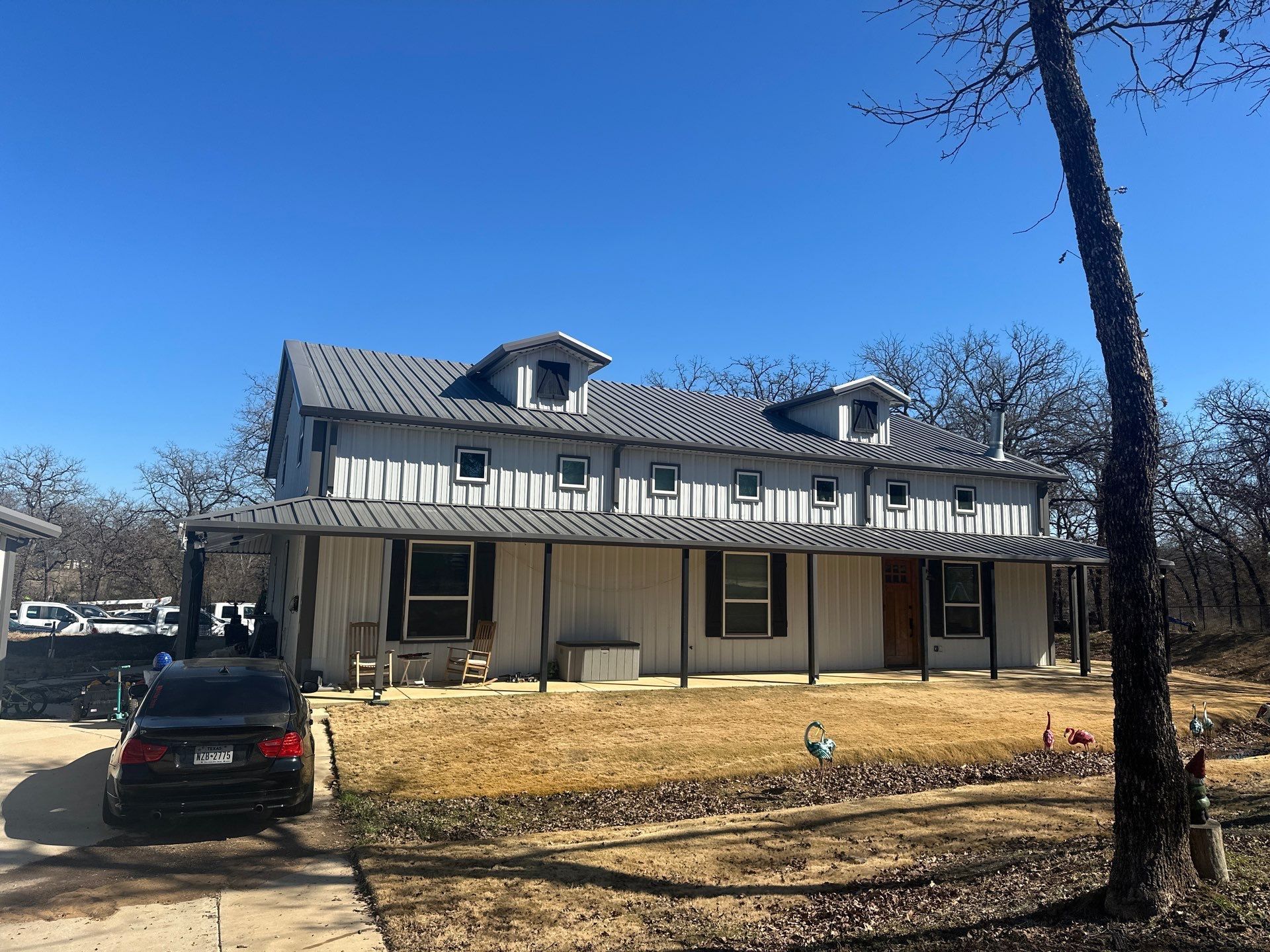 Two-story gray house with a front porch, parked car, and bare trees under a clear blue sky