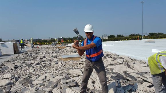 Worker in hard hat and orange vest breaking rubble on a construction site under a clear sky