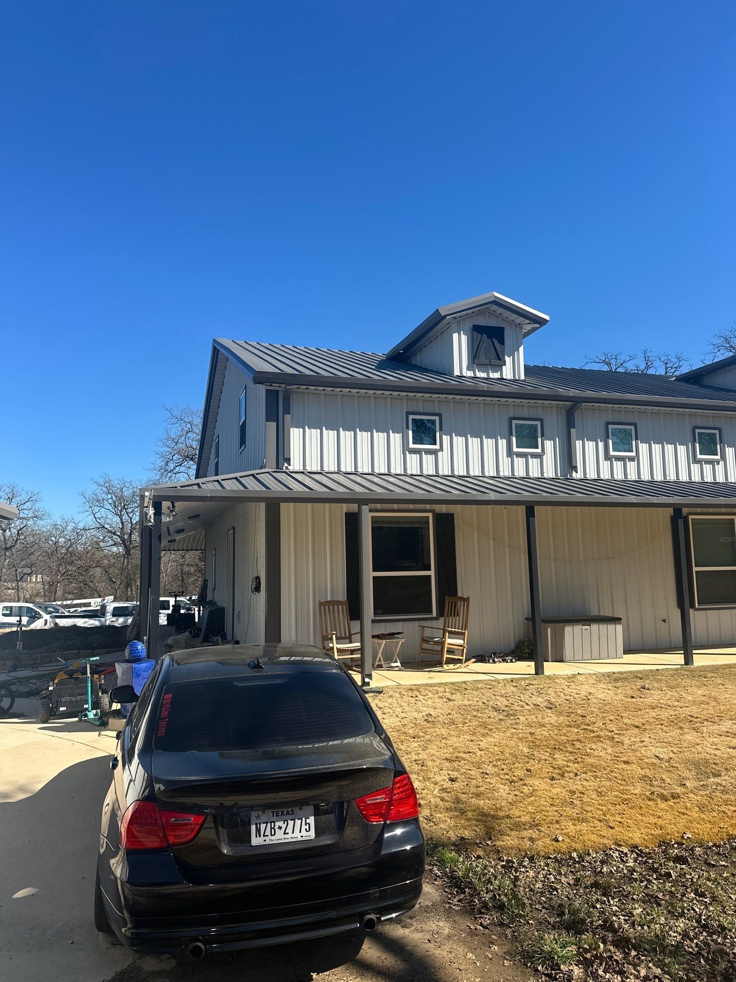 Black sedan parked in front of a beige house with a porch under a clear blue sky