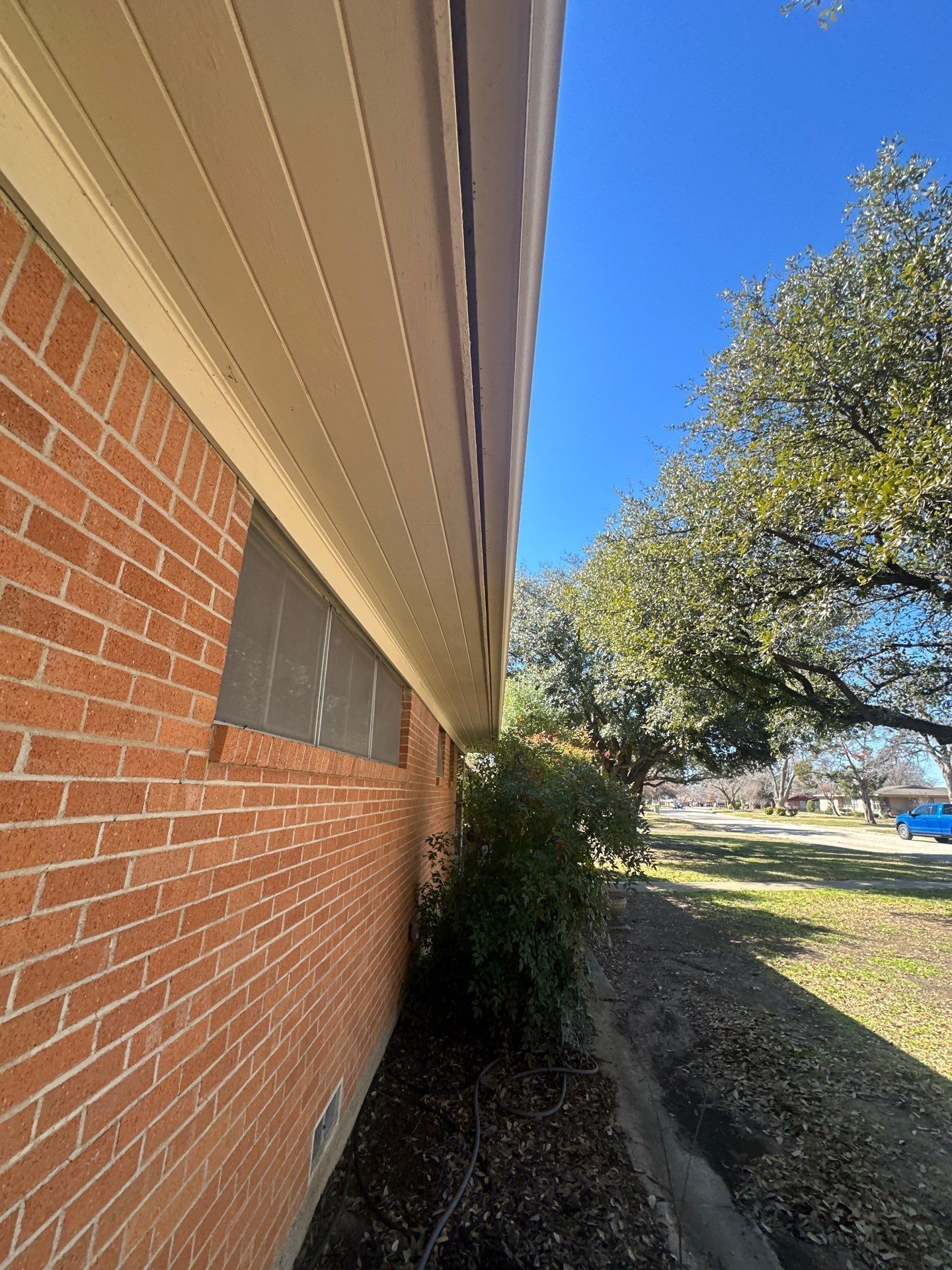 Brick house side yard with a window, shrubs, and a sunny grassy lawn under a blue sky.