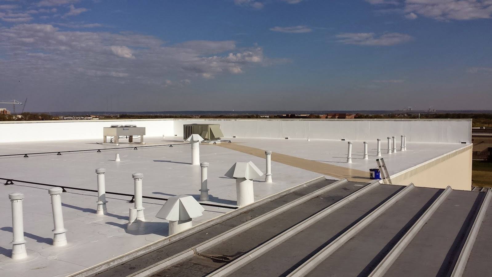 Rooftop with white HVAC units and vents under a cloudy sky