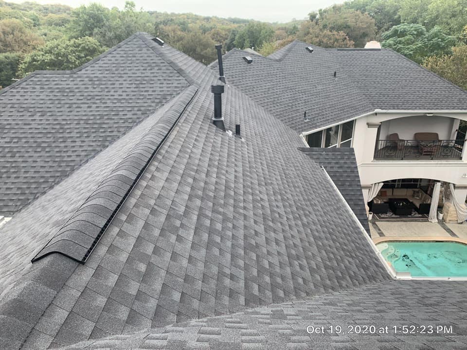 Aerial view of a dark gray shingle roof with chimneys beside a house and backyard pool.