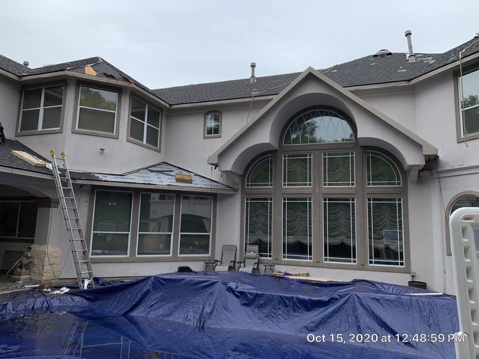 Back of a two-story gray house with large windows and a blue tarp-covered patio under construction