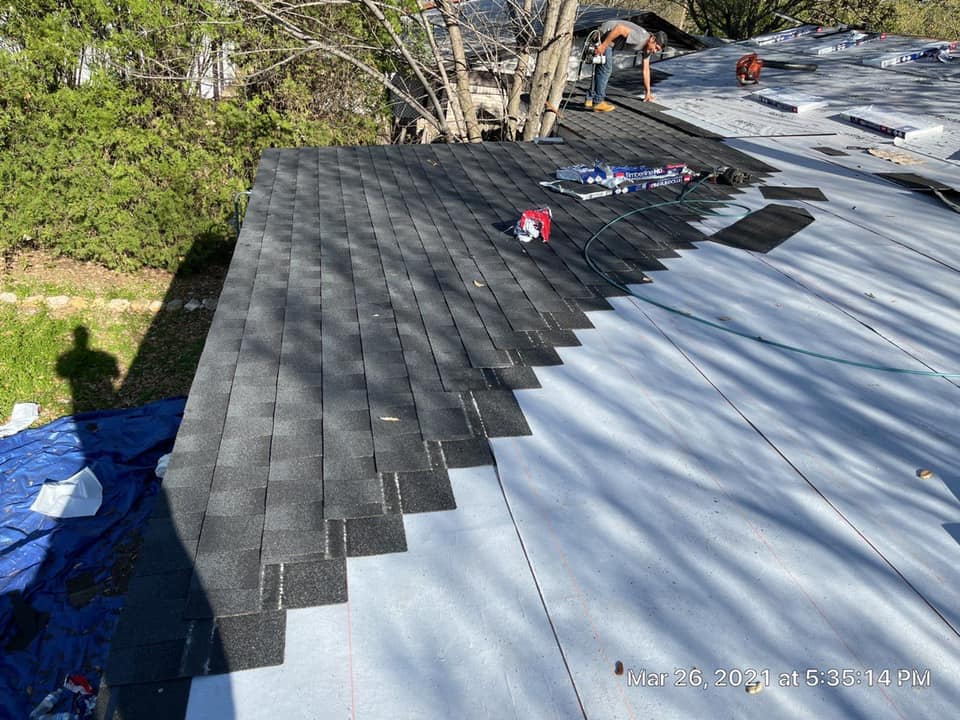 Roof under construction with black shingles over silver underlayment and workers near the ridge