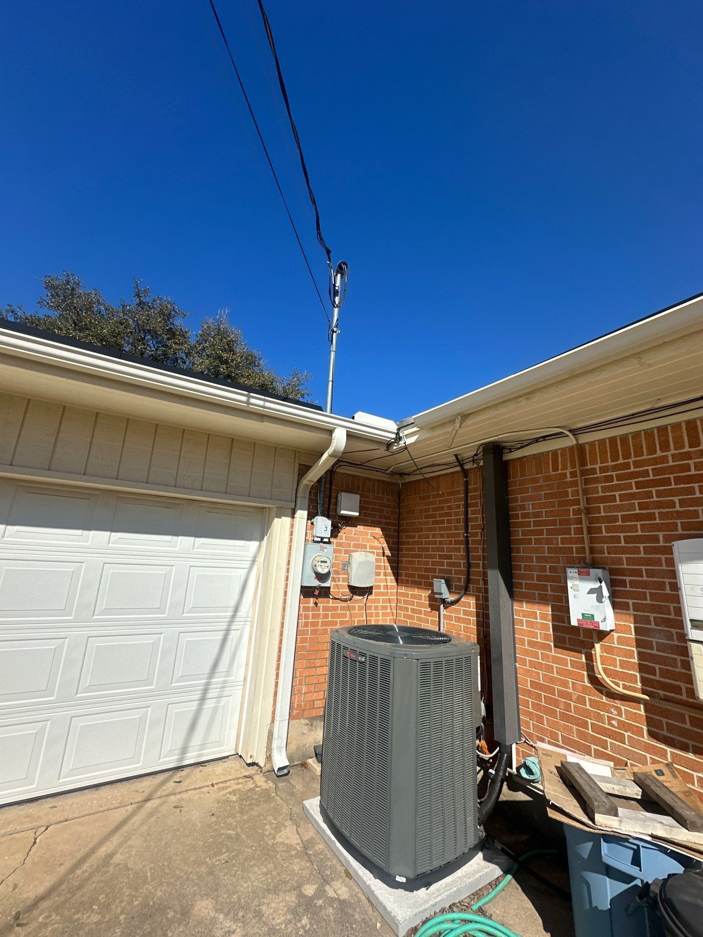 Outdoor air conditioner unit beside a brick house and white garage door under a clear blue sky