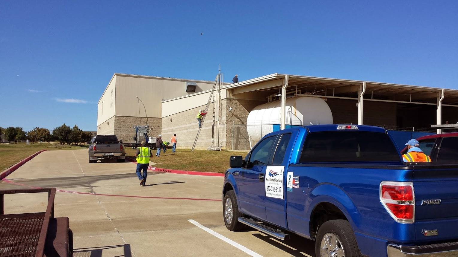 Blue pickup truck parked outside a building, with a worker in a high-visibility vest nearby.