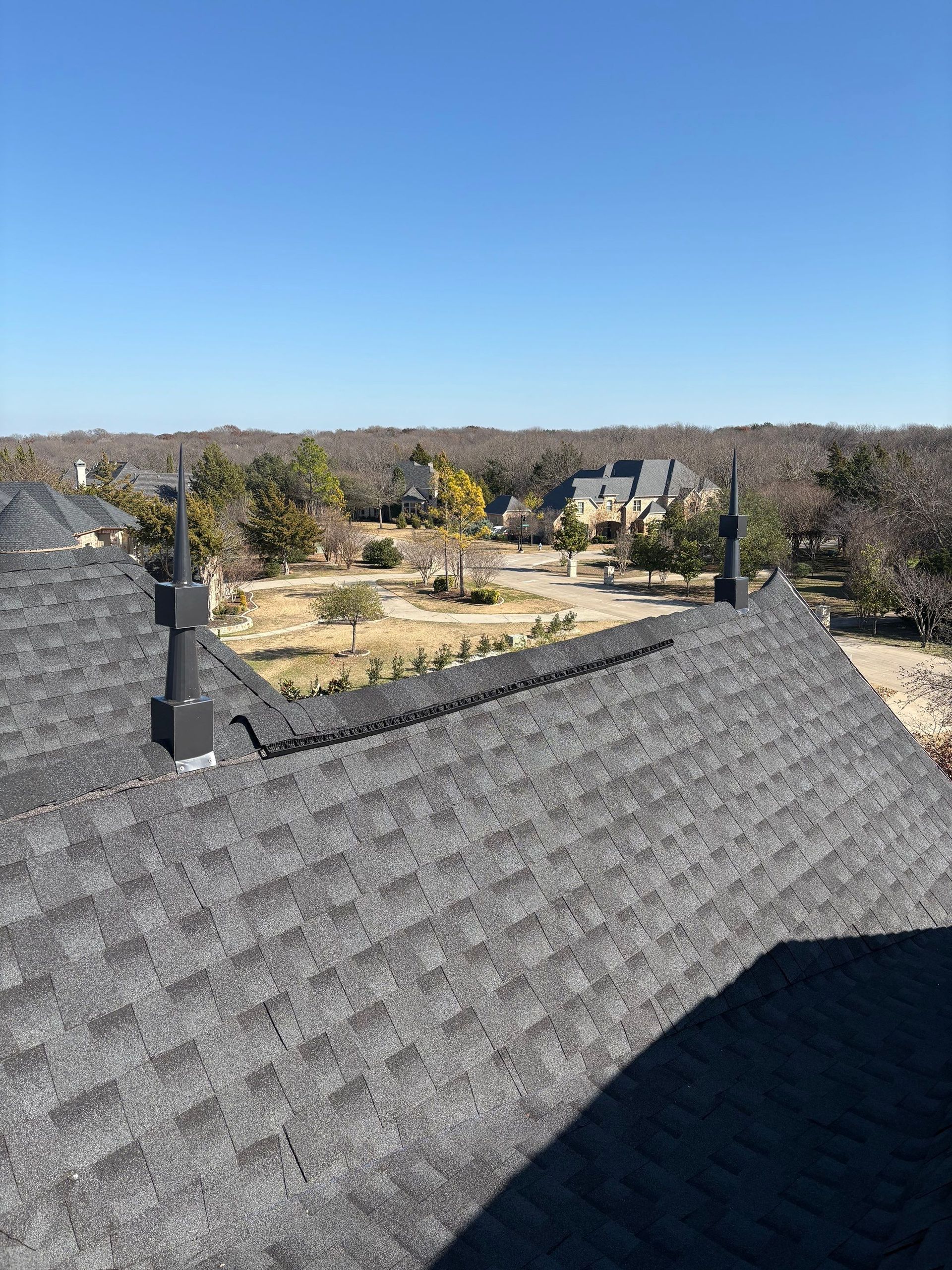 Rooftop view over a residential neighborhood, with dark gray shingles and a clear blue sky.