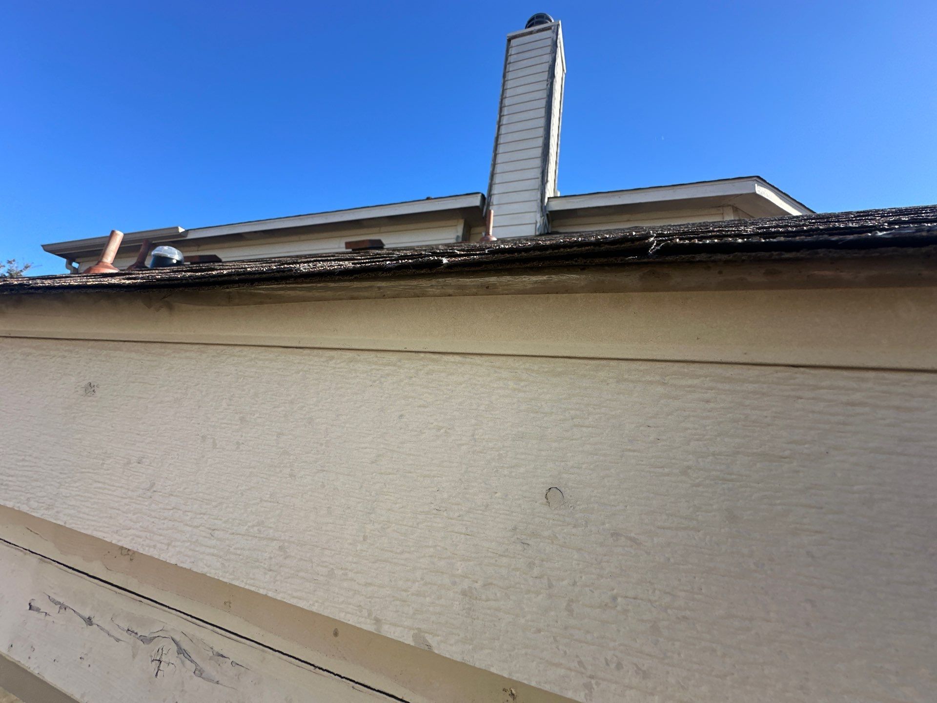 White exterior wall and roofline with a chimney against a bright blue sky.