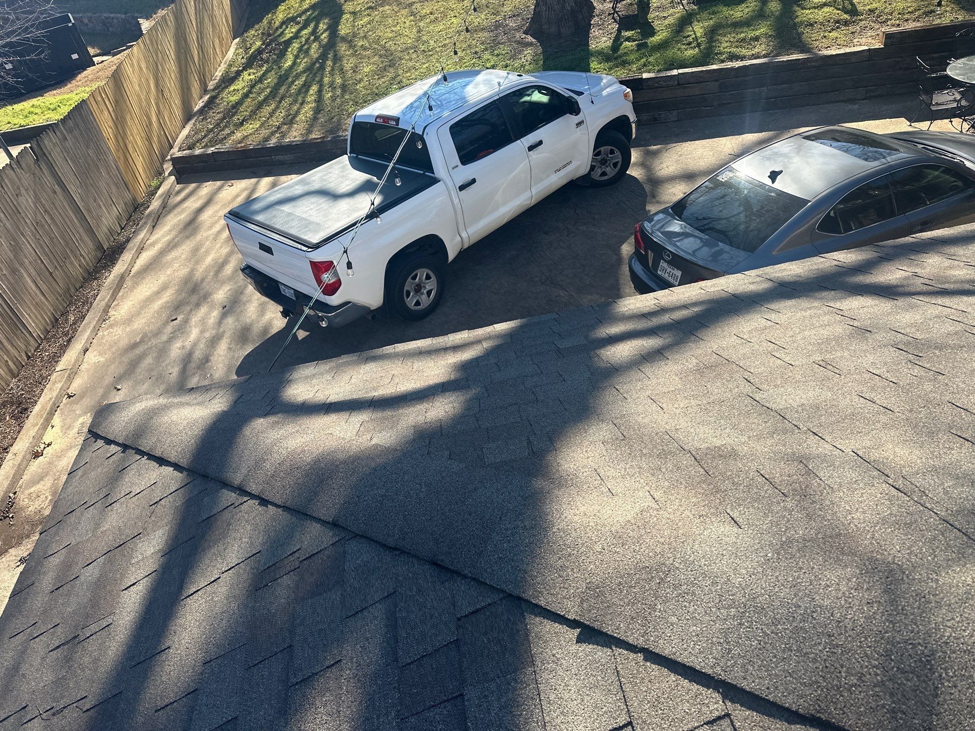 White pickup truck parked beside a silver car on a steep paved driveway, viewed from above