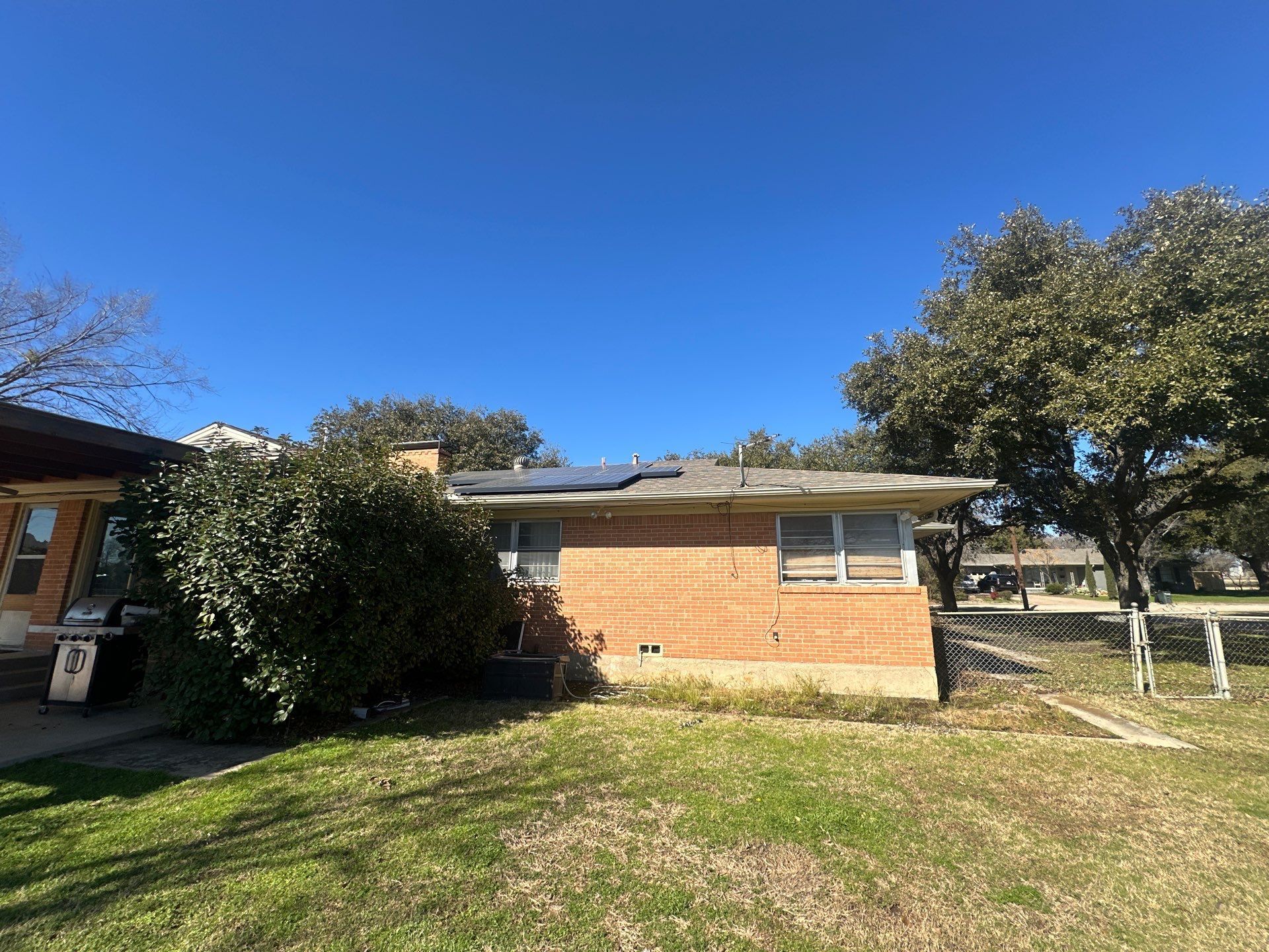 Brick house with white windows and a yard under a clear blue sky