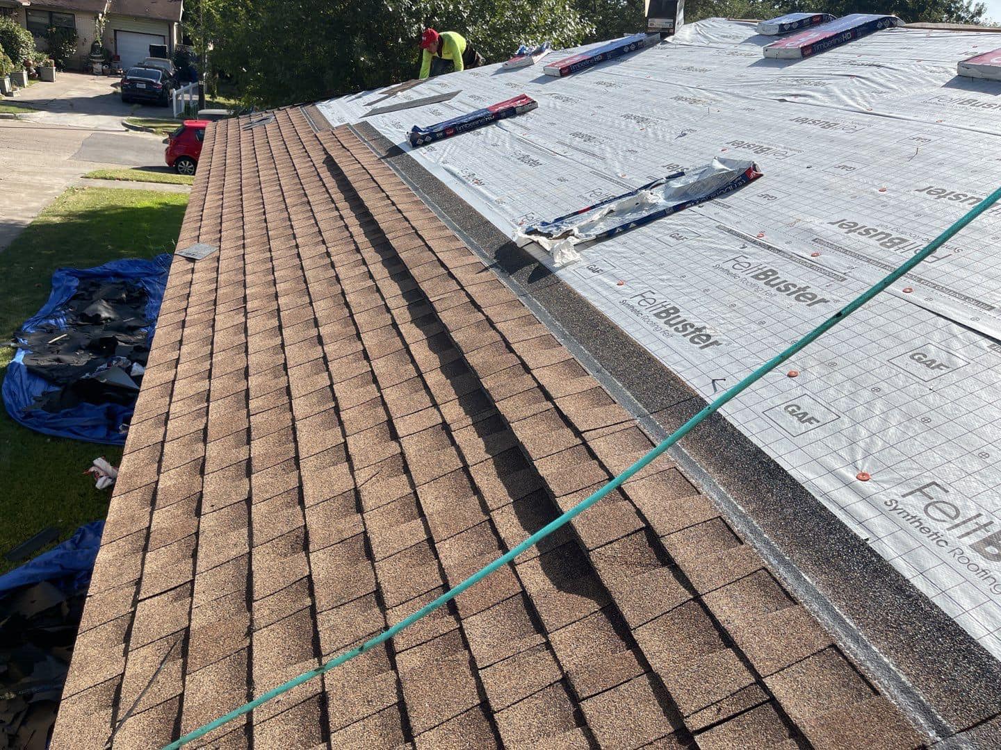 Roofing shingles being installed, with brown shingles on one side and underlayment on the other.