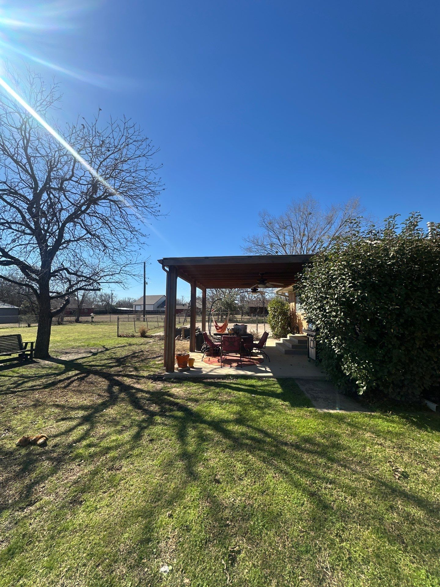 Sunny backyard with a wooden pergola, grass lawn, and trees casting long shadows