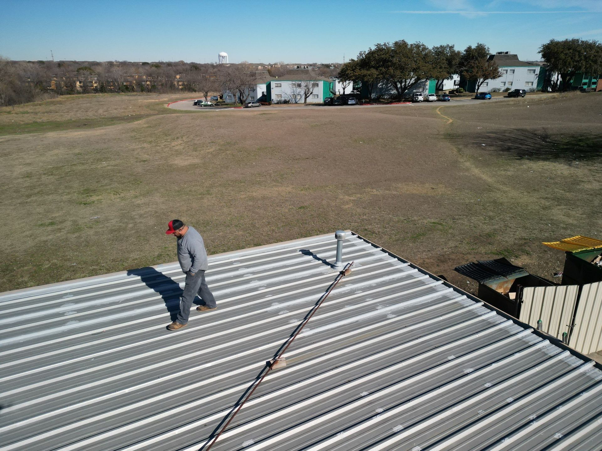 Worker on a corrugated metal roof, looking over a wide grassy field on a clear day