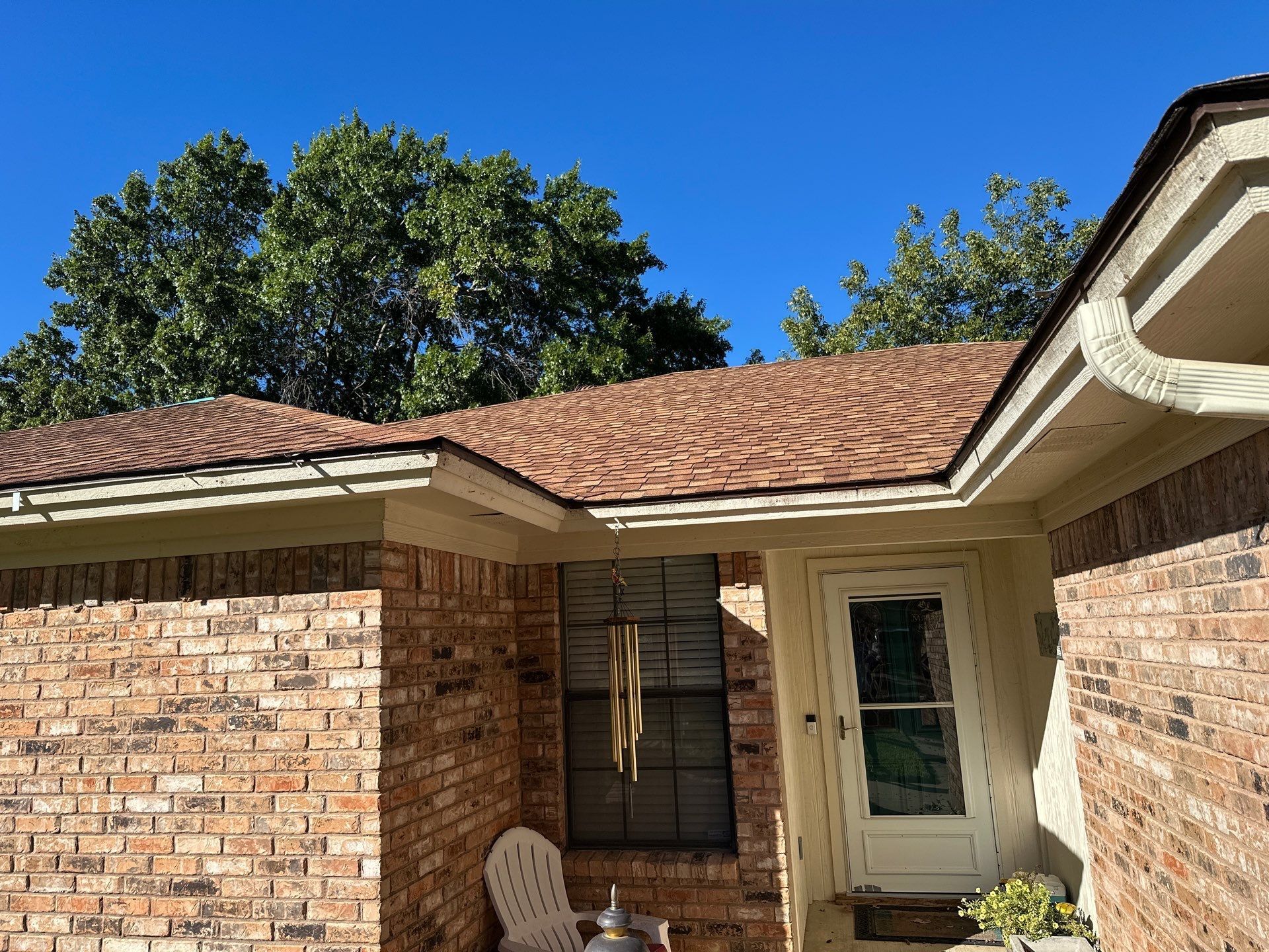 Brick house patio with beige chair, white door, and red-tile roof under a blue sky