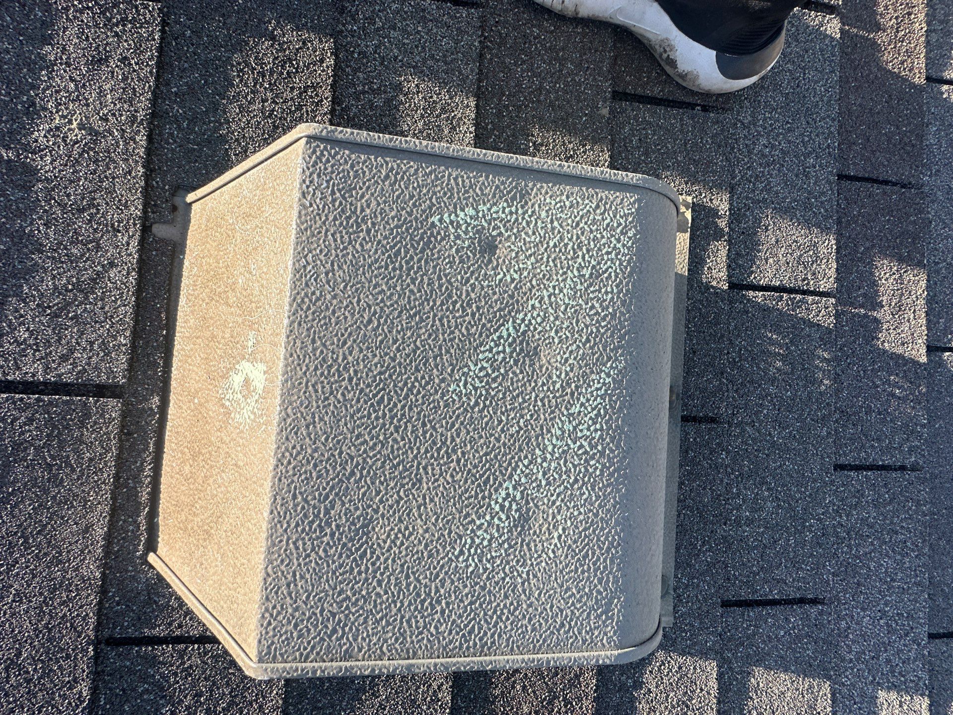 Close-up of a metal roof vent with a round cap on gray asphalt shingles.