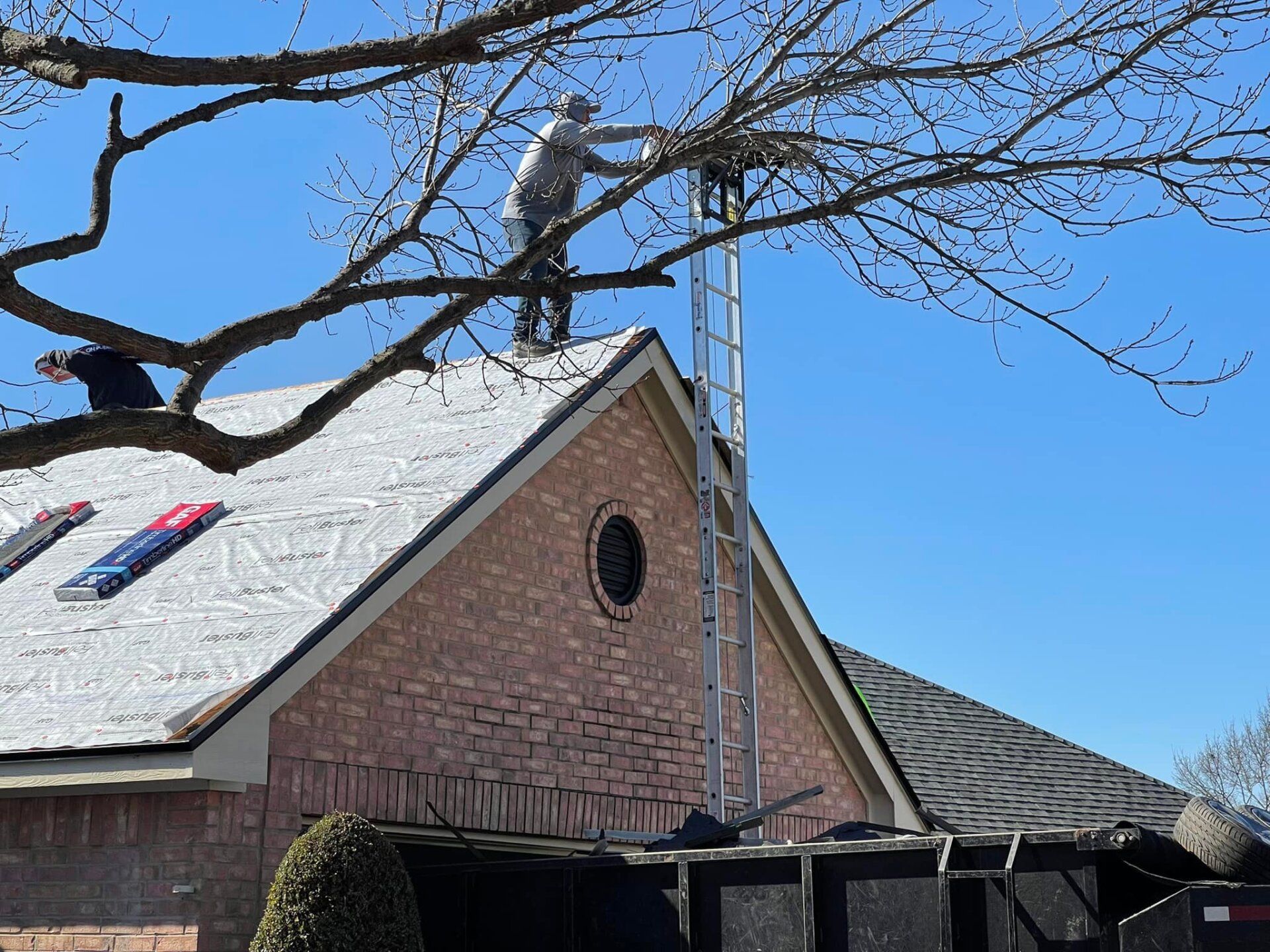 Worker on a roof using a ladder near a brick house under a clear blue sky