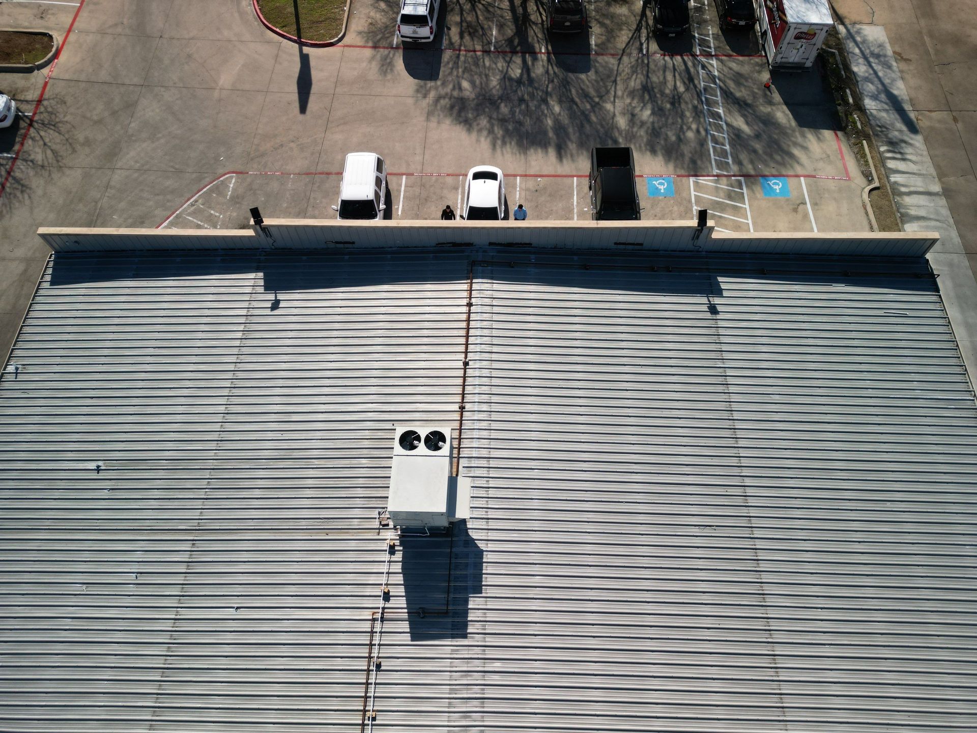 Aerial view of a gray rooftop with a central vent, parking lot, and a few cars at the top edge