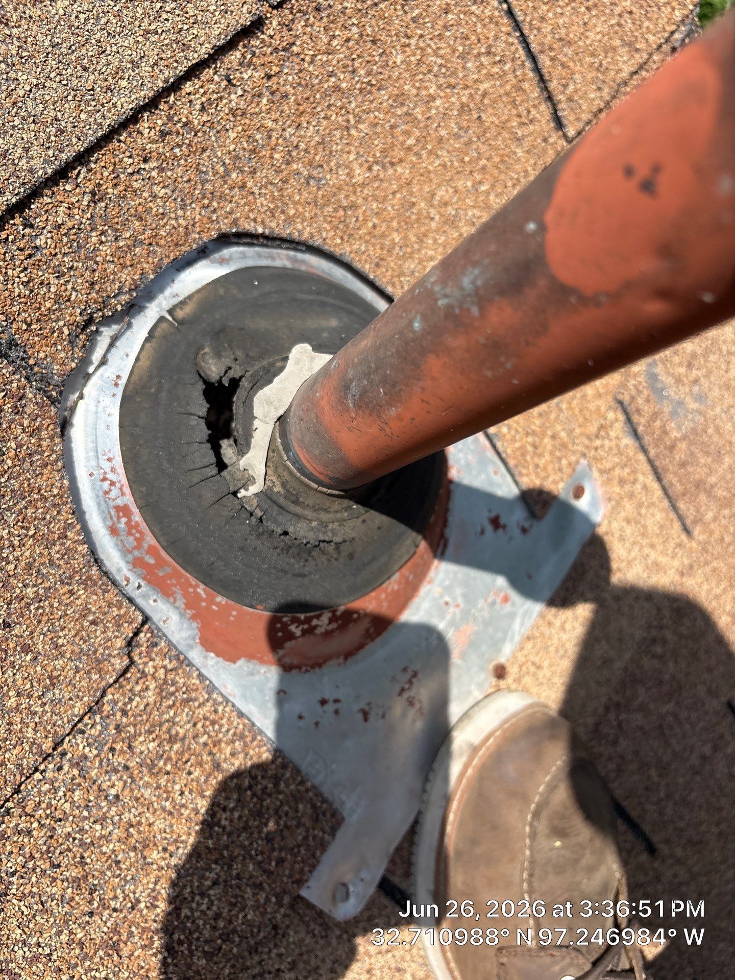 Rusty pipe vent on a shingled roof with damaged flashing around the base.