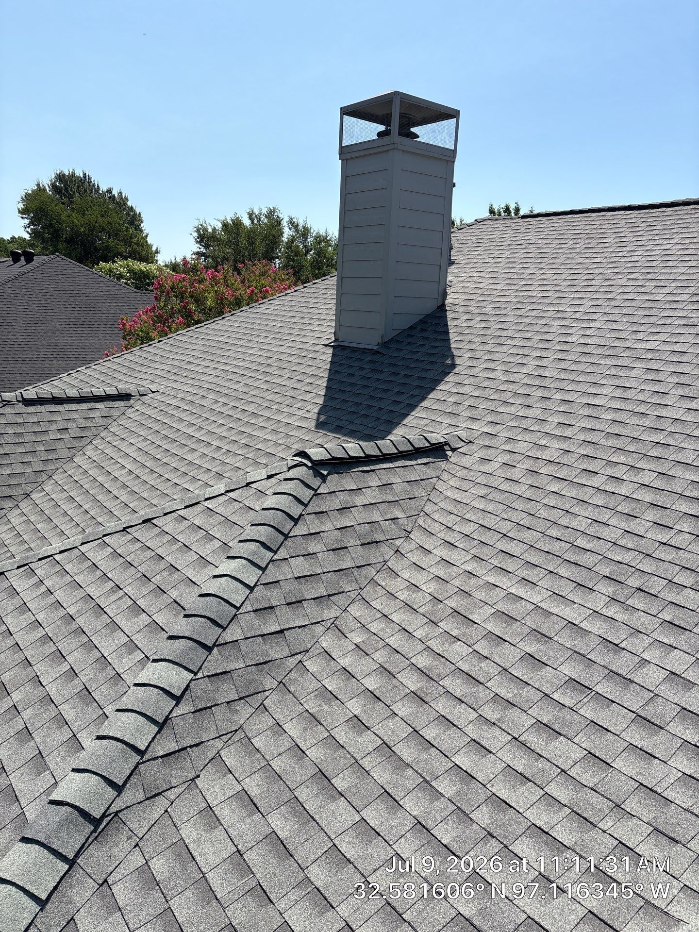 Rooftop with gray shingles and a central white chimney under a clear blue sky
