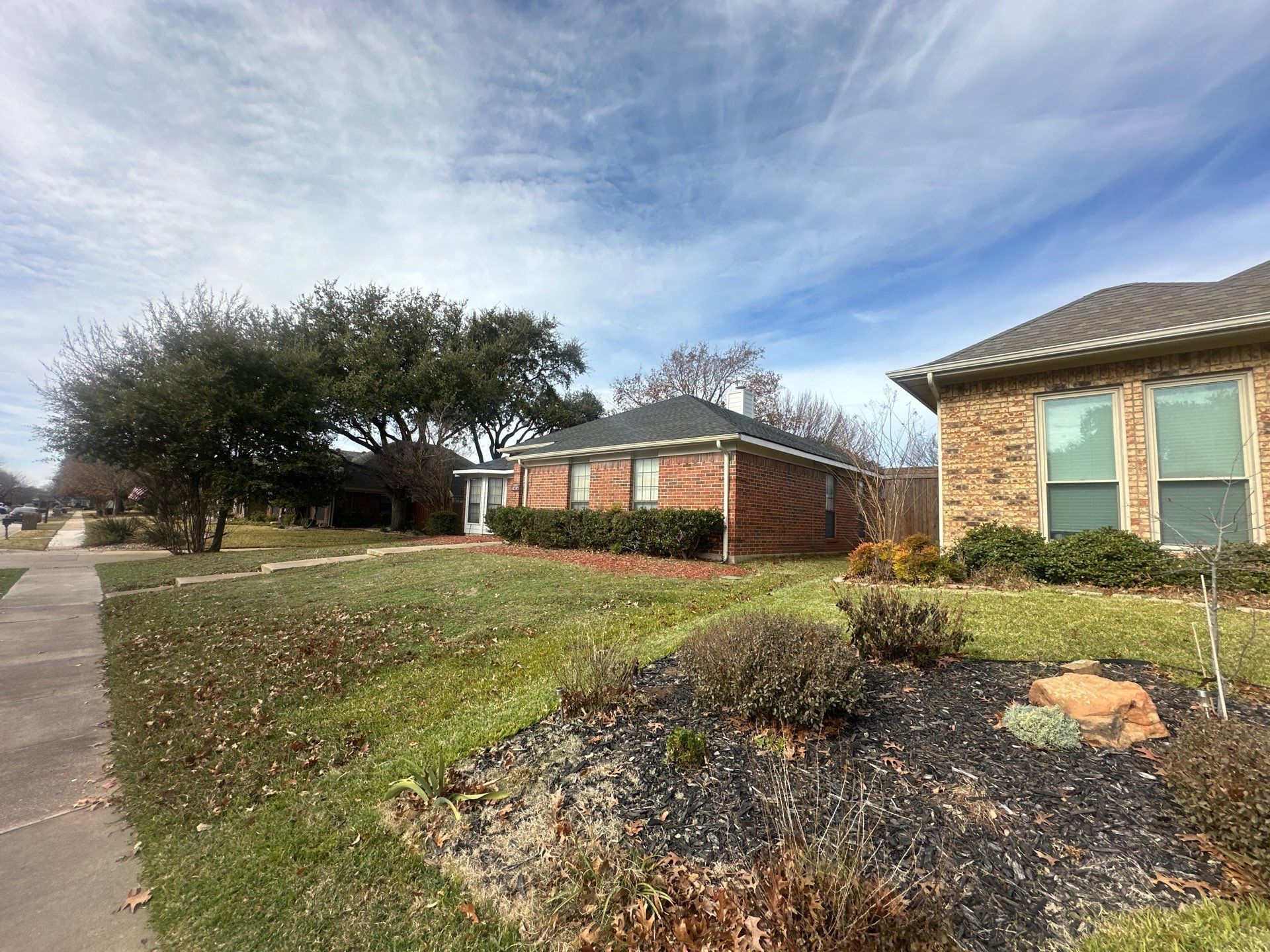 Suburban houses with stone facades beside a sidewalk and landscaped front yards under a cloudy sky