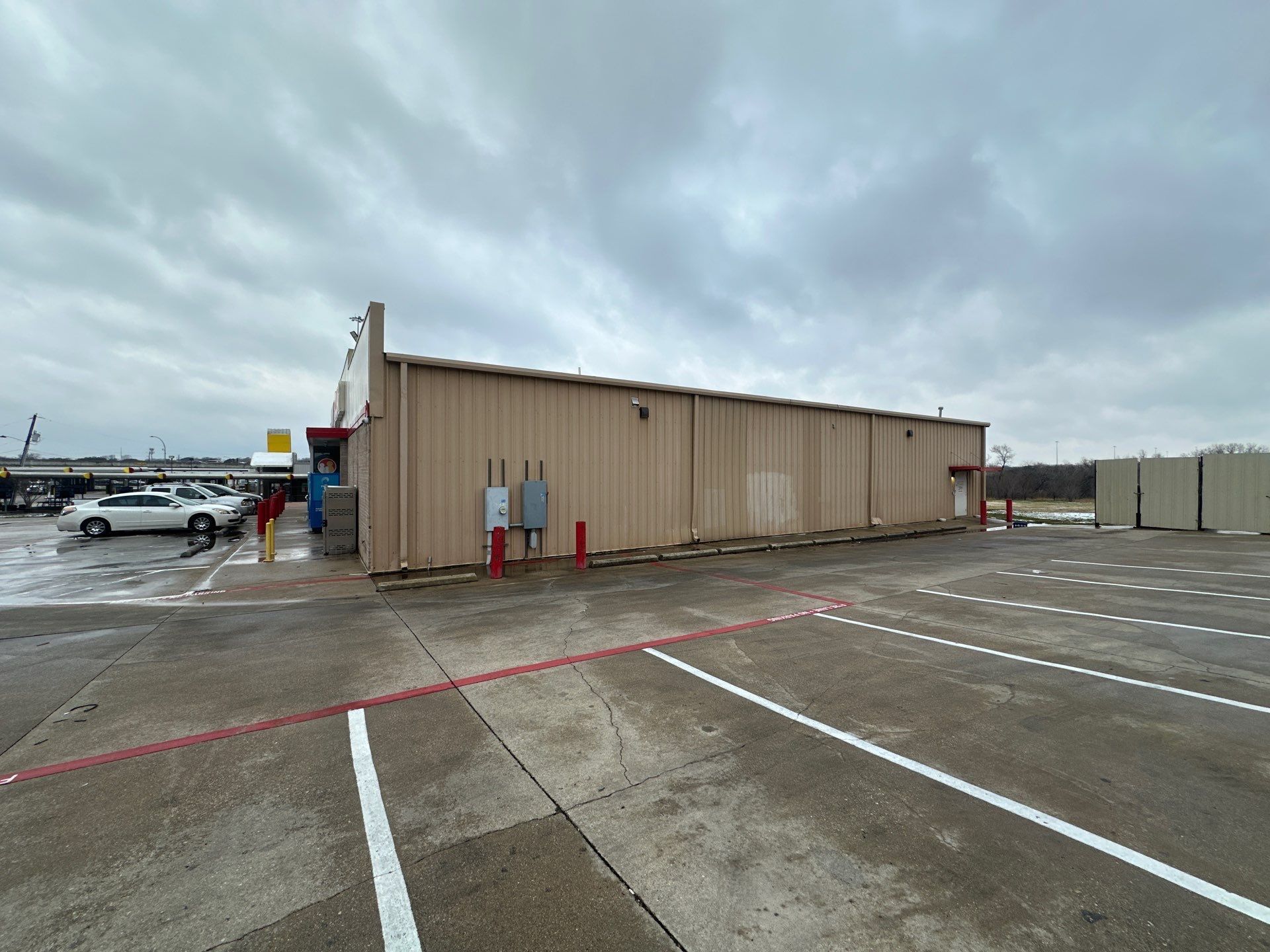 Beige shipping container in a wet parking lot under cloudy skies, with white lane markings and a few people nearby