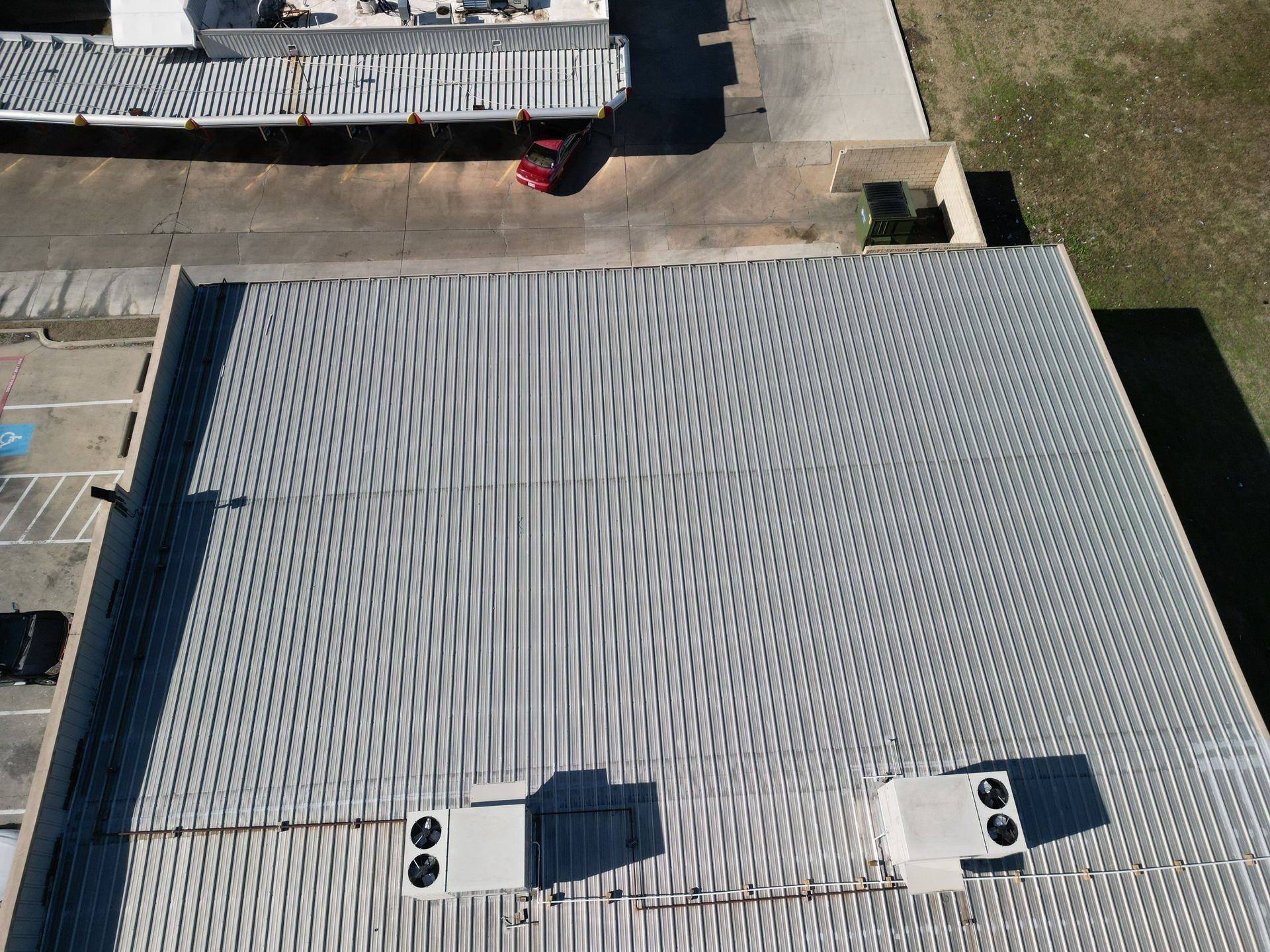 Aerial view of a gray corrugated roof with vents and surrounding pavement and grass
