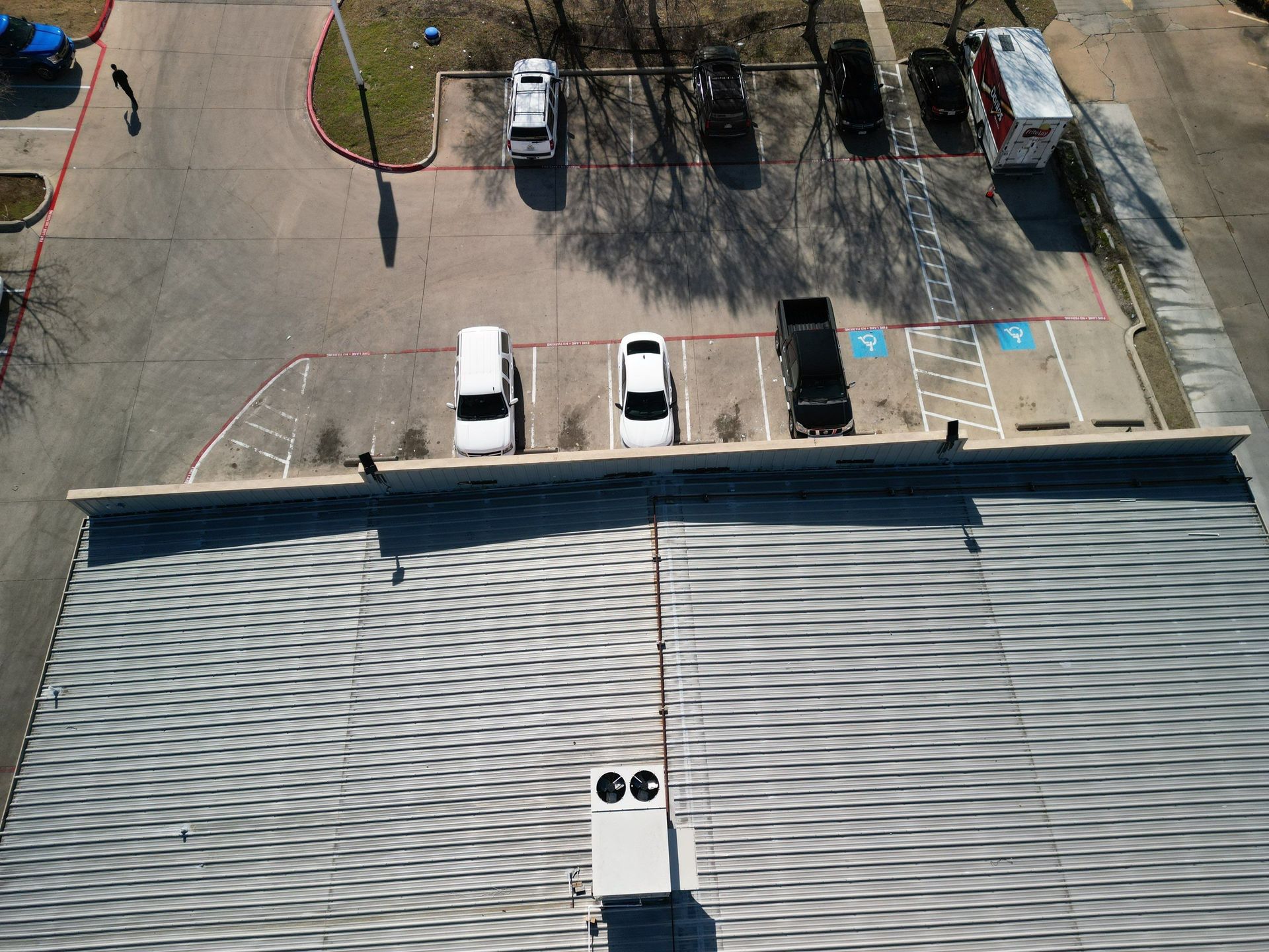 Aerial view of a rooftop and parking lot with several parked cars and blue accessible parking spaces.
