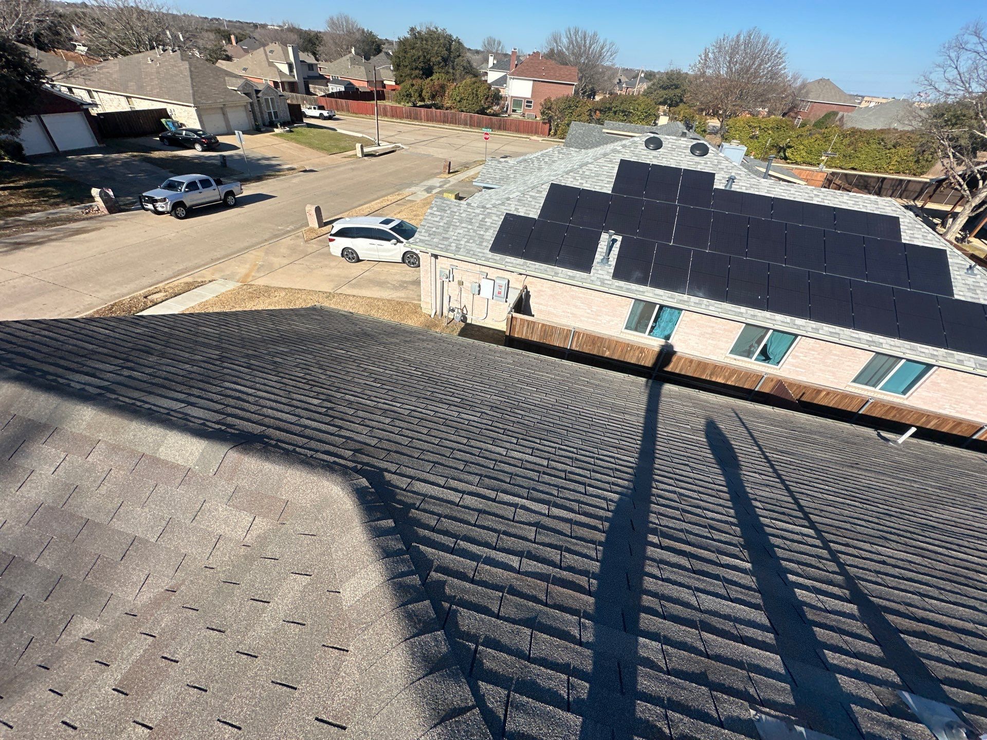 Rooftop solar panels on a house in a suburban neighborhood, with neighboring homes and a street below.