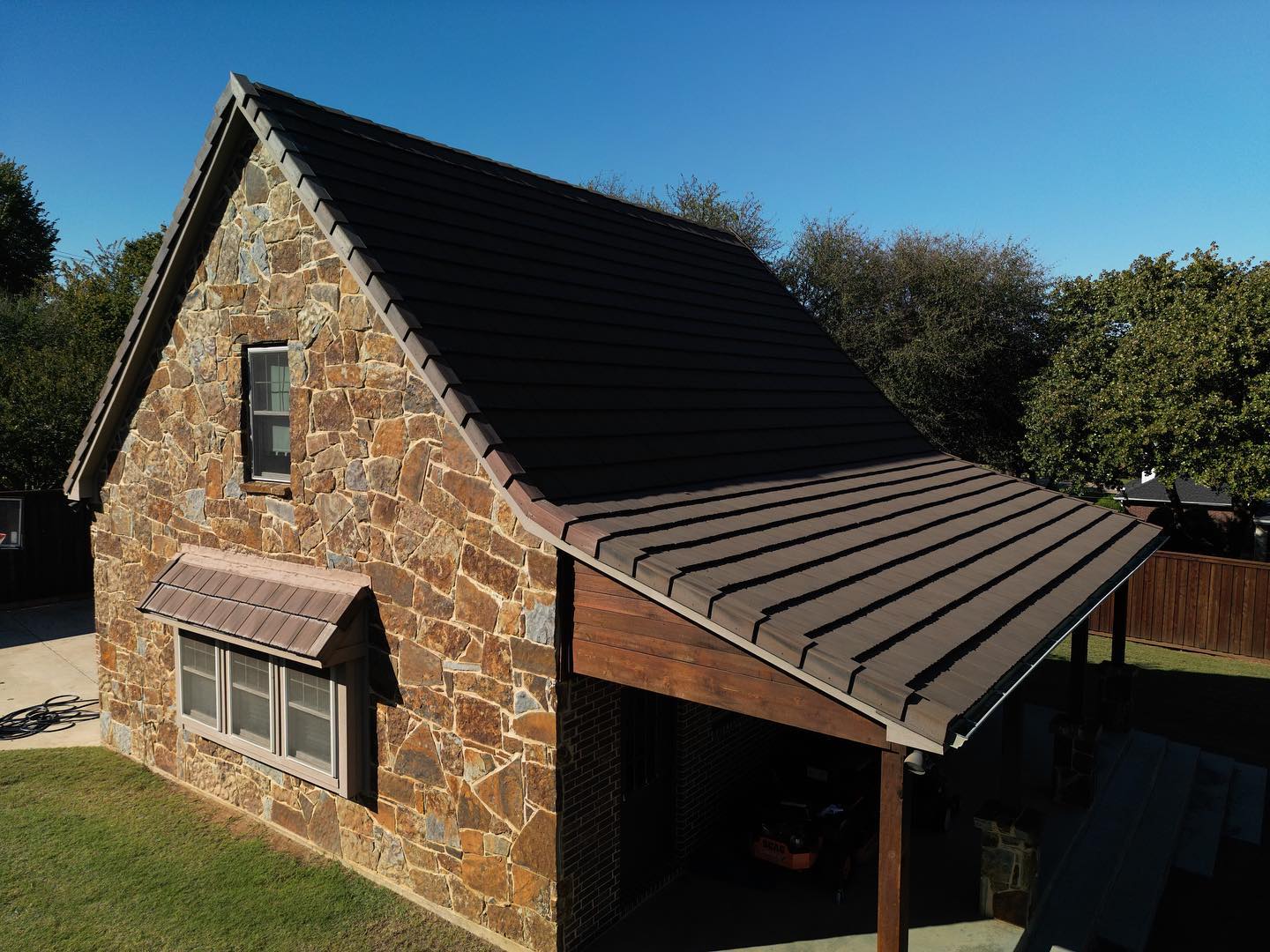 Stone cottage with a brown metal roof and covered porch in a sunny outdoor setting