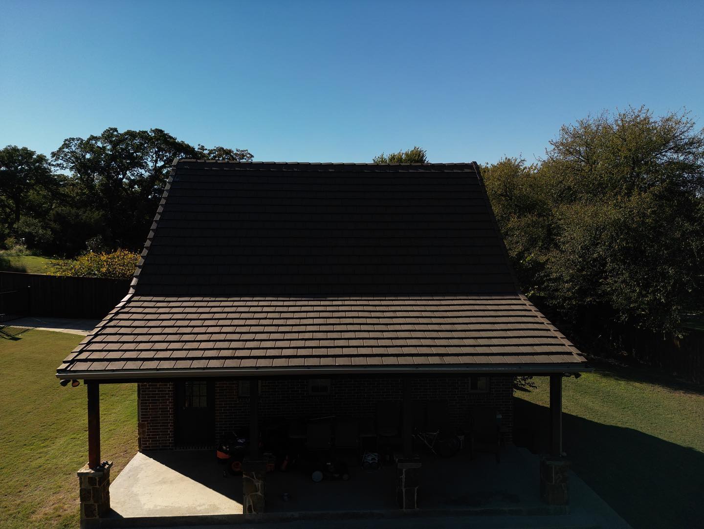 Small open-sided wooden pavilion with a dark sloped roof in a sunny grassy yard.