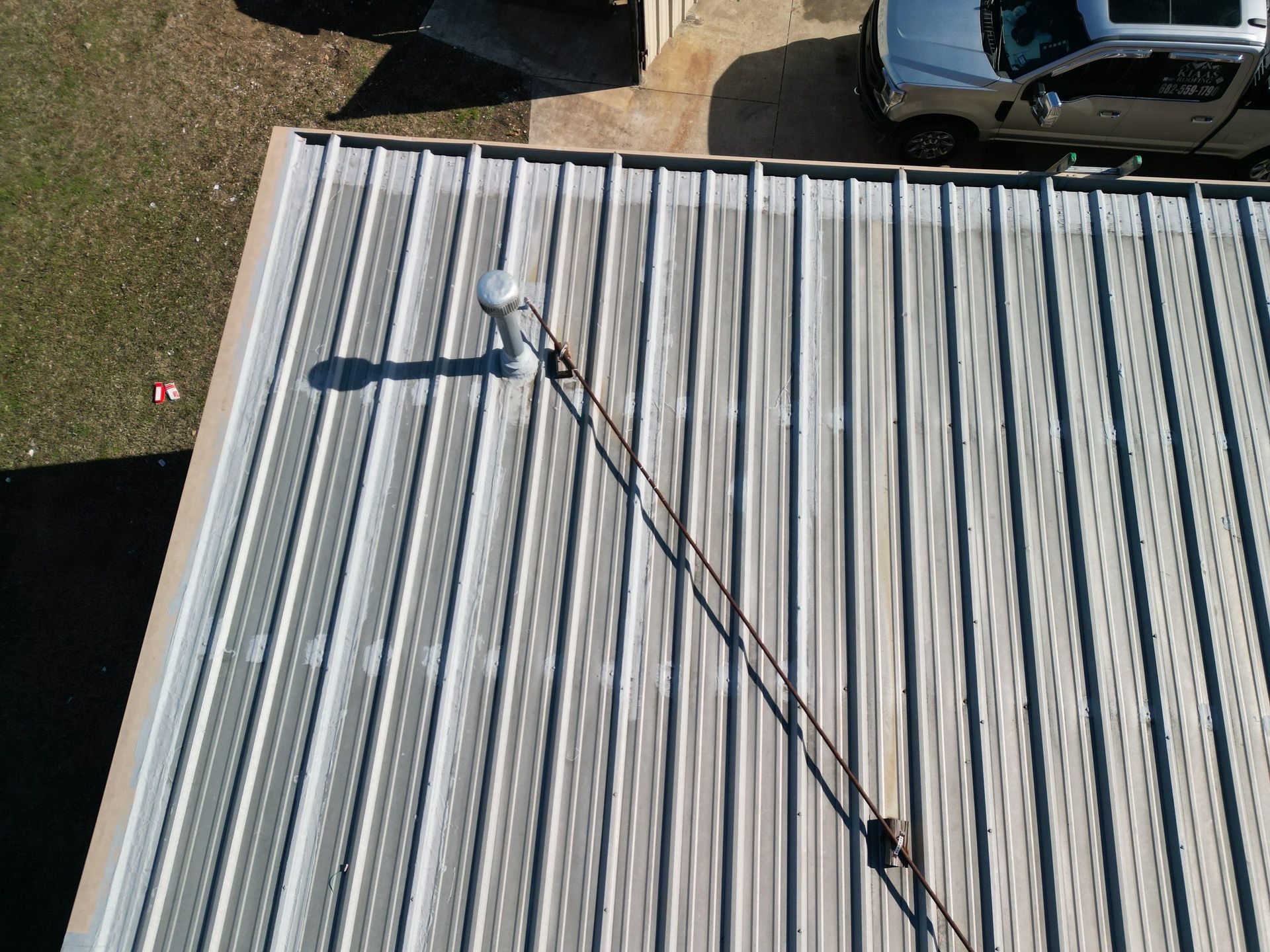 Roofer on a metal roof, using a safety line near parked vehicles below.