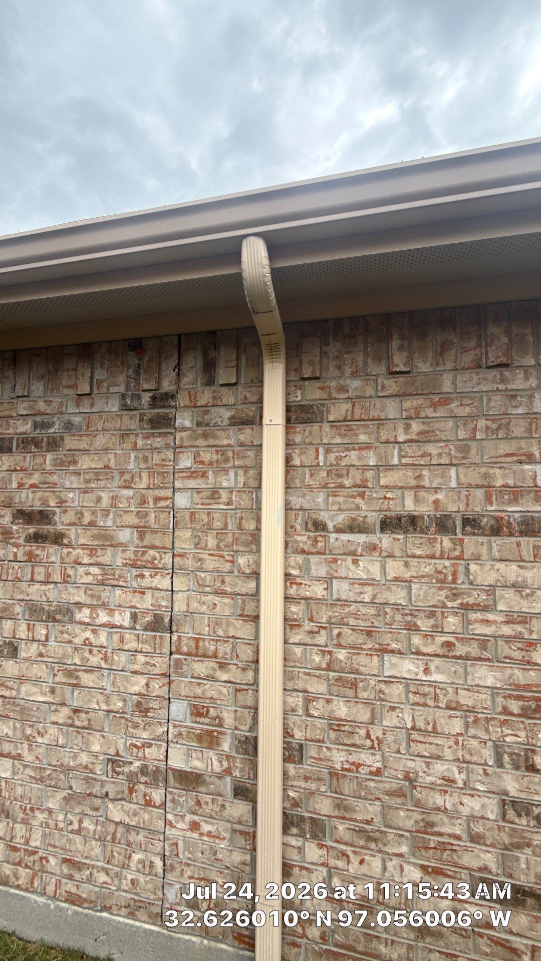 Brick house exterior with a downspout bent under the roofline and extending down the wall