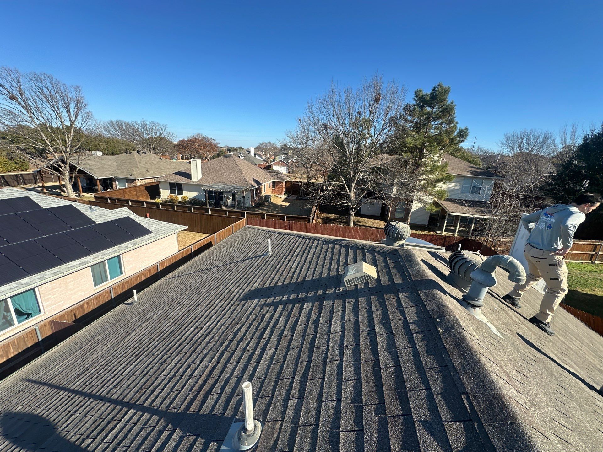 Workers on a shingled roof inspecting damage in a suburban neighborhood