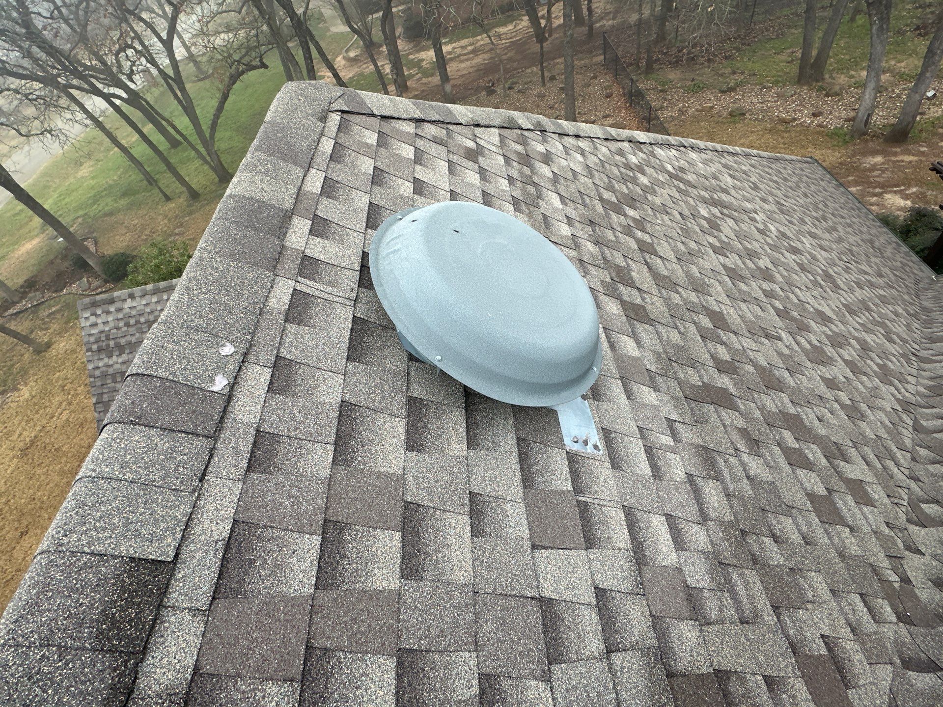 Blue roof vent on gray shingle roof with leafless trees in the background