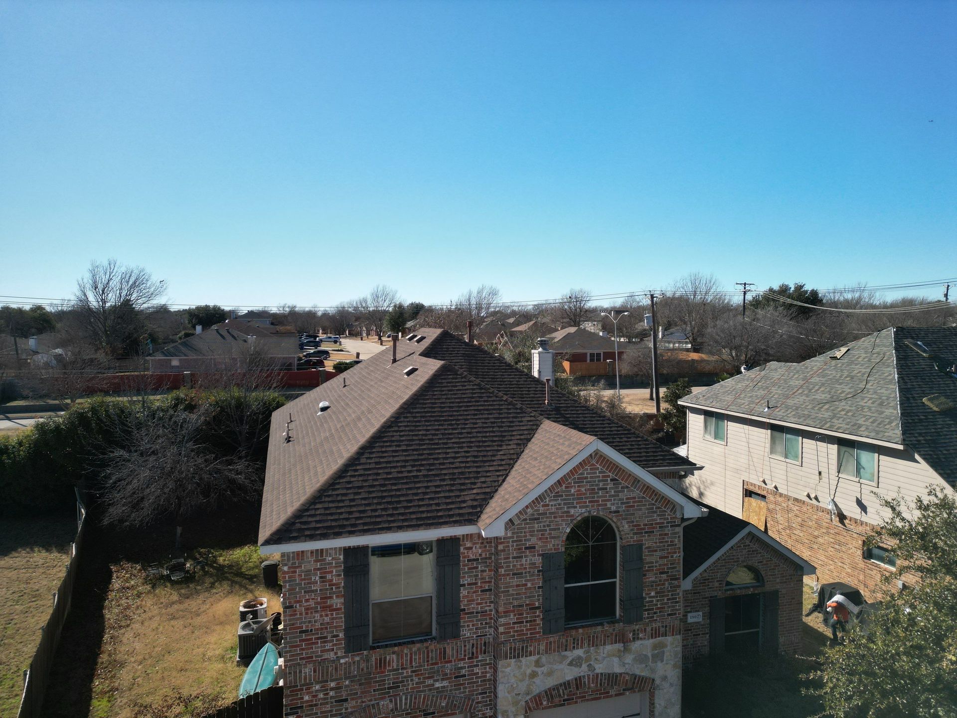 Suburban brick house with brown roof and small front yard under a clear blue sky