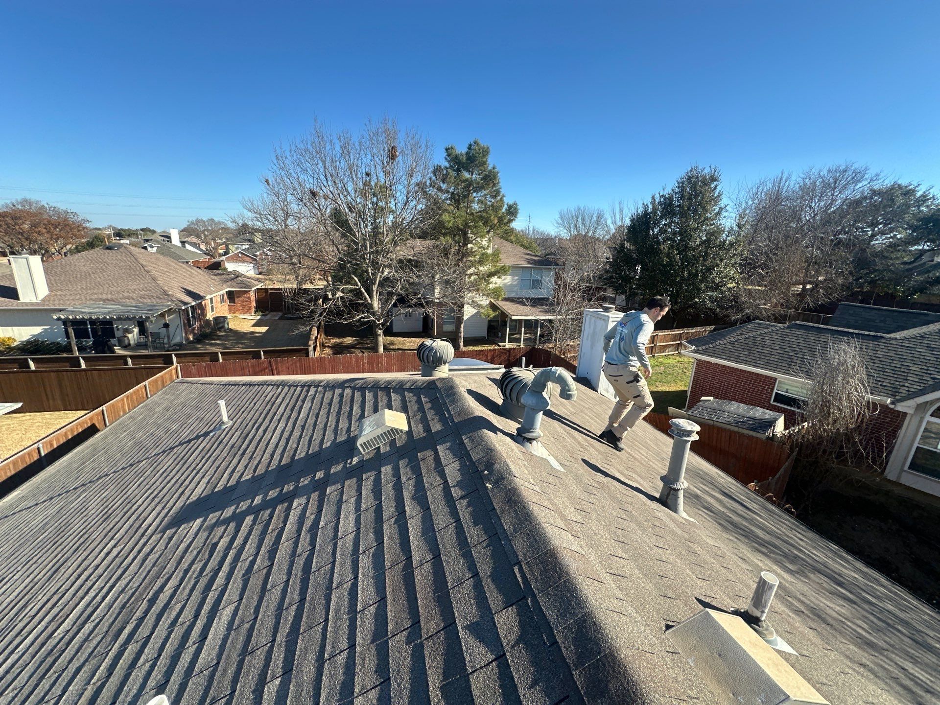 People working on a flat rooftop under a clear blue sky, with tools and nearby houses visible.